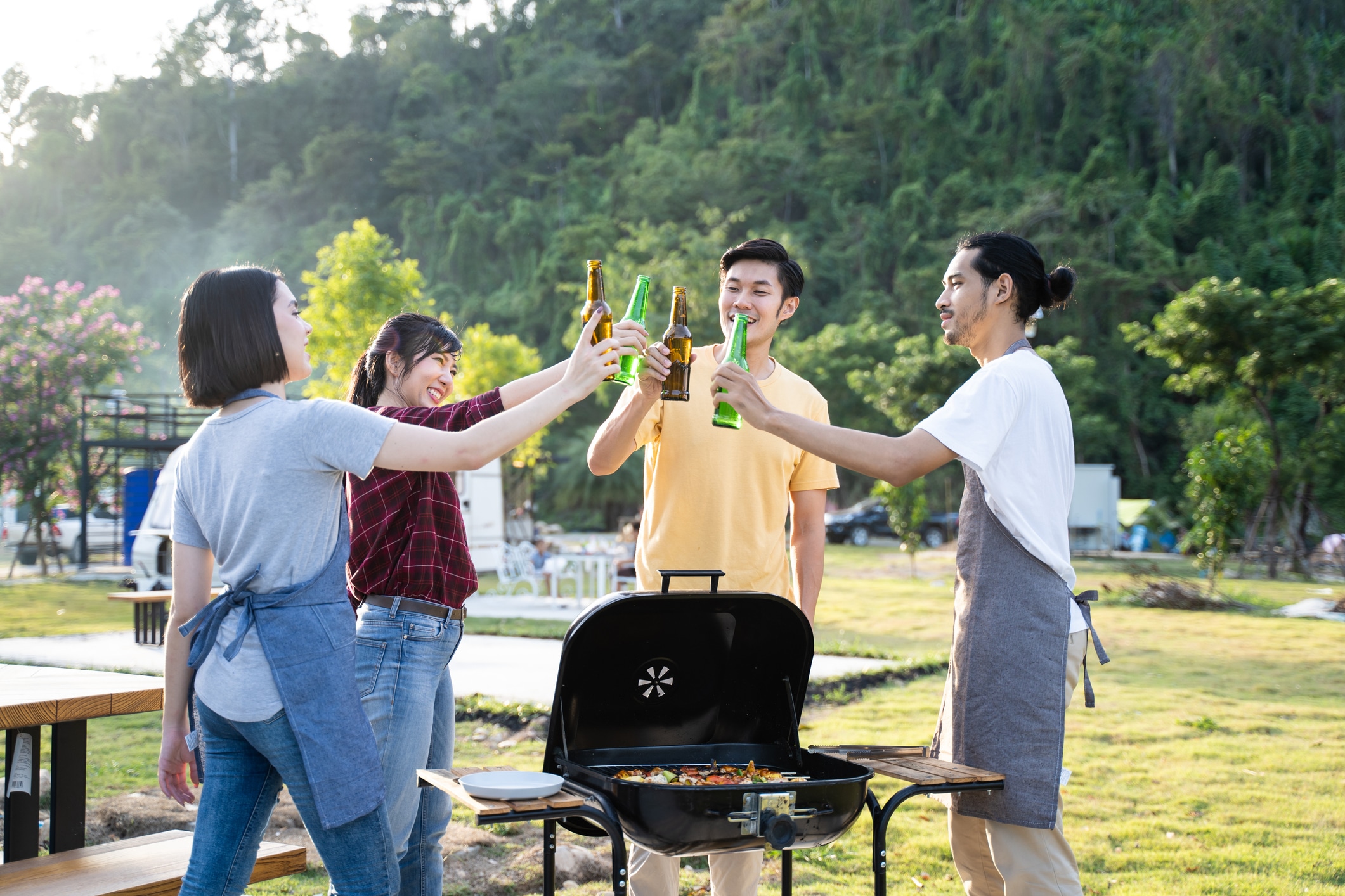 Two couples toast beers during outdoor barbecue.