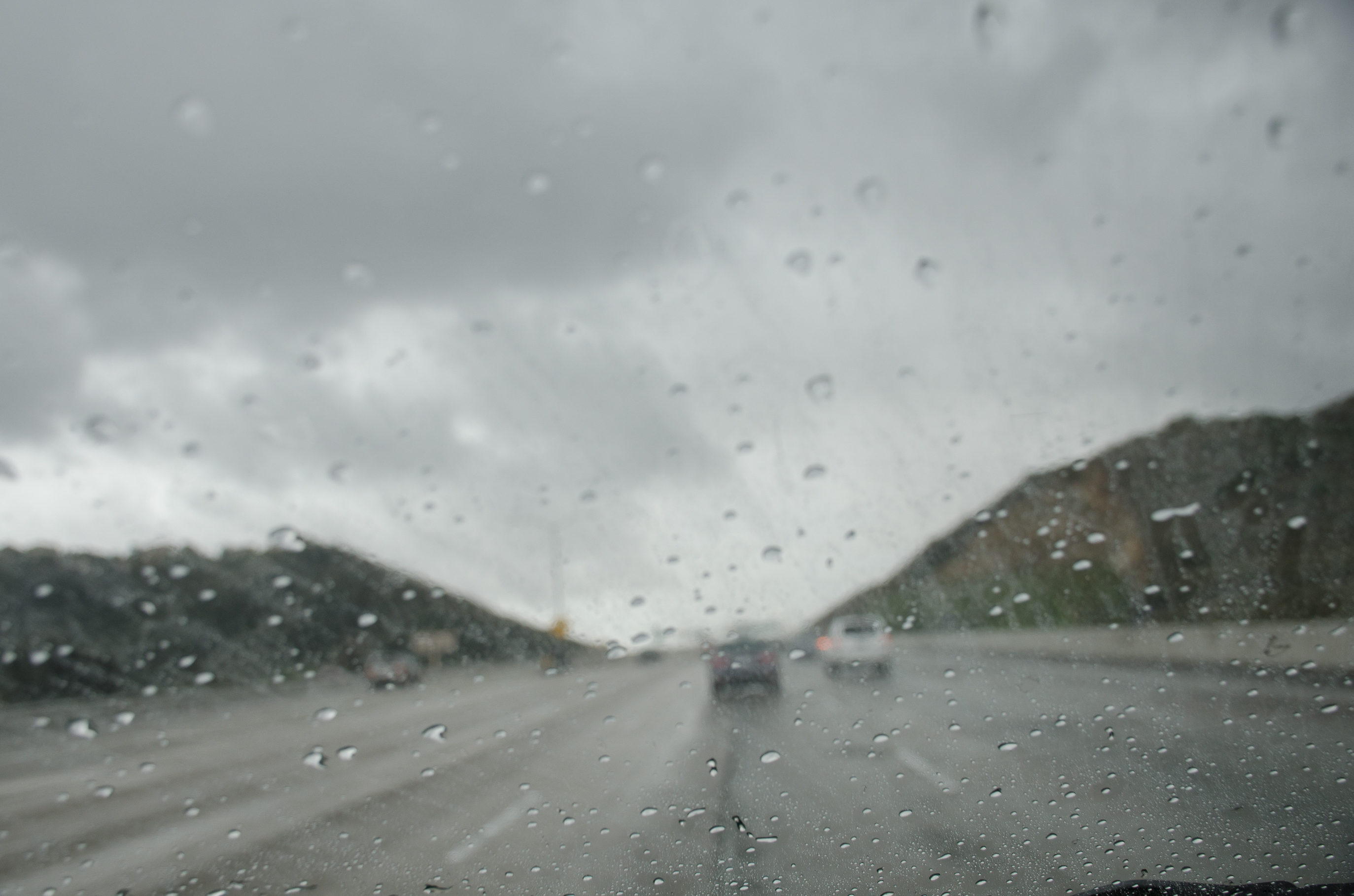 Cars driving on the freeway on a mountainous pass in rainy weather.