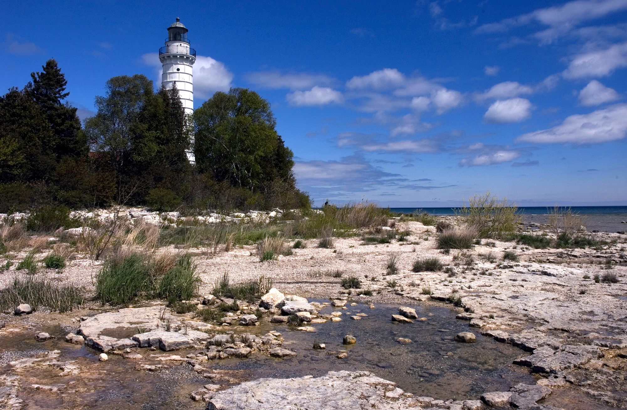A white lighthouse towers over a rocky shore.