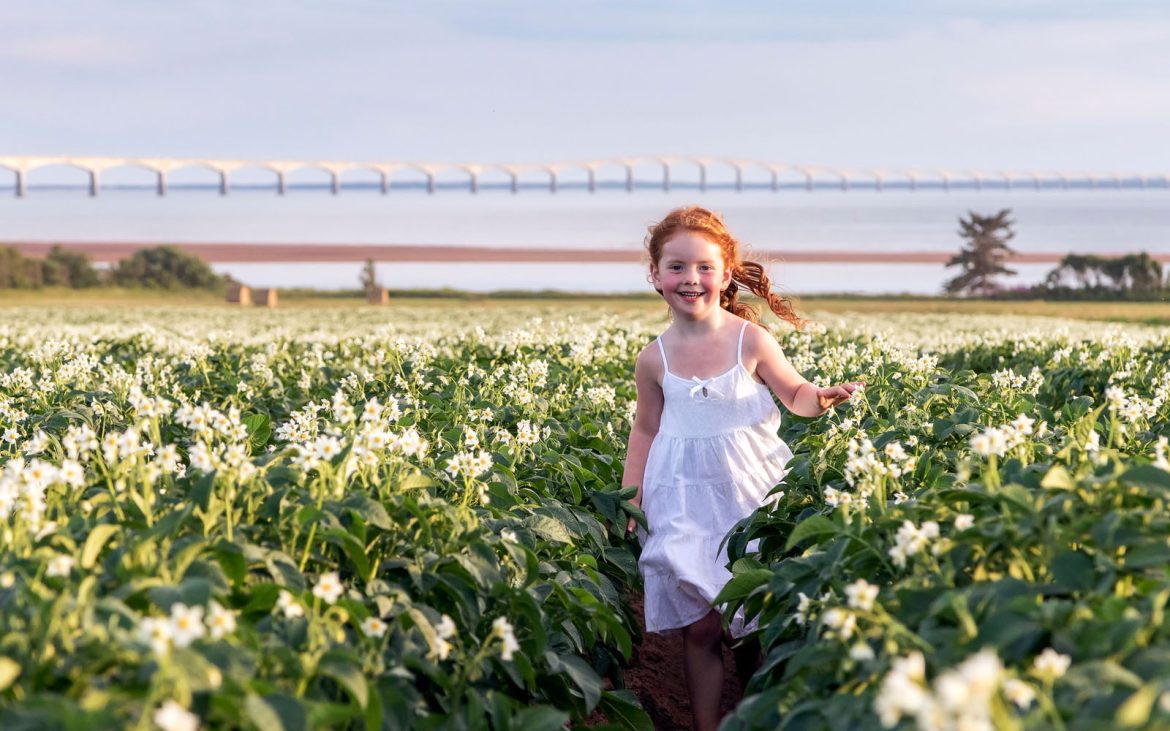 A girl plays in a field of green flowers with ocean in background.