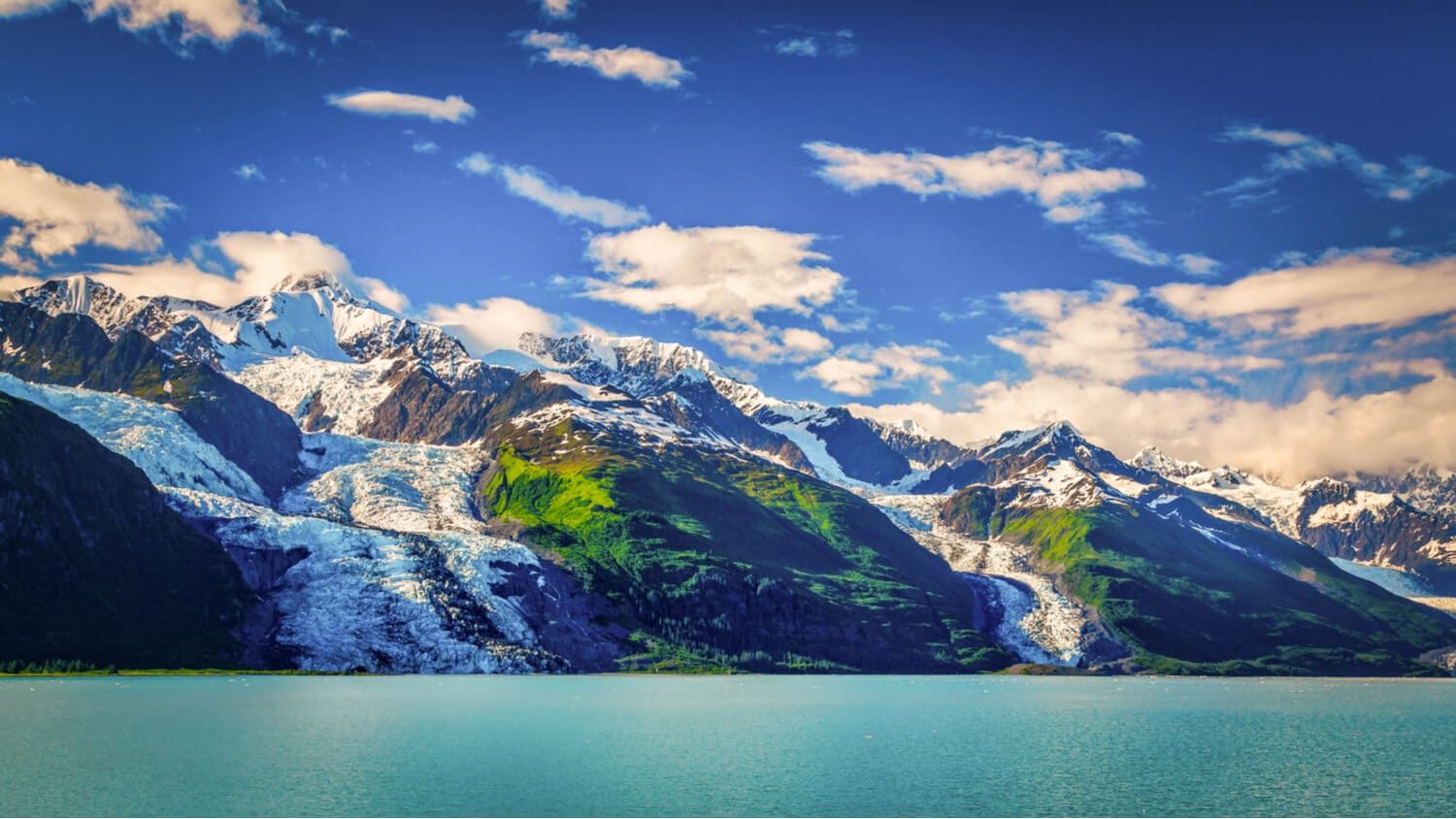 A glacier rises from the shore of a emerald-hued lake.