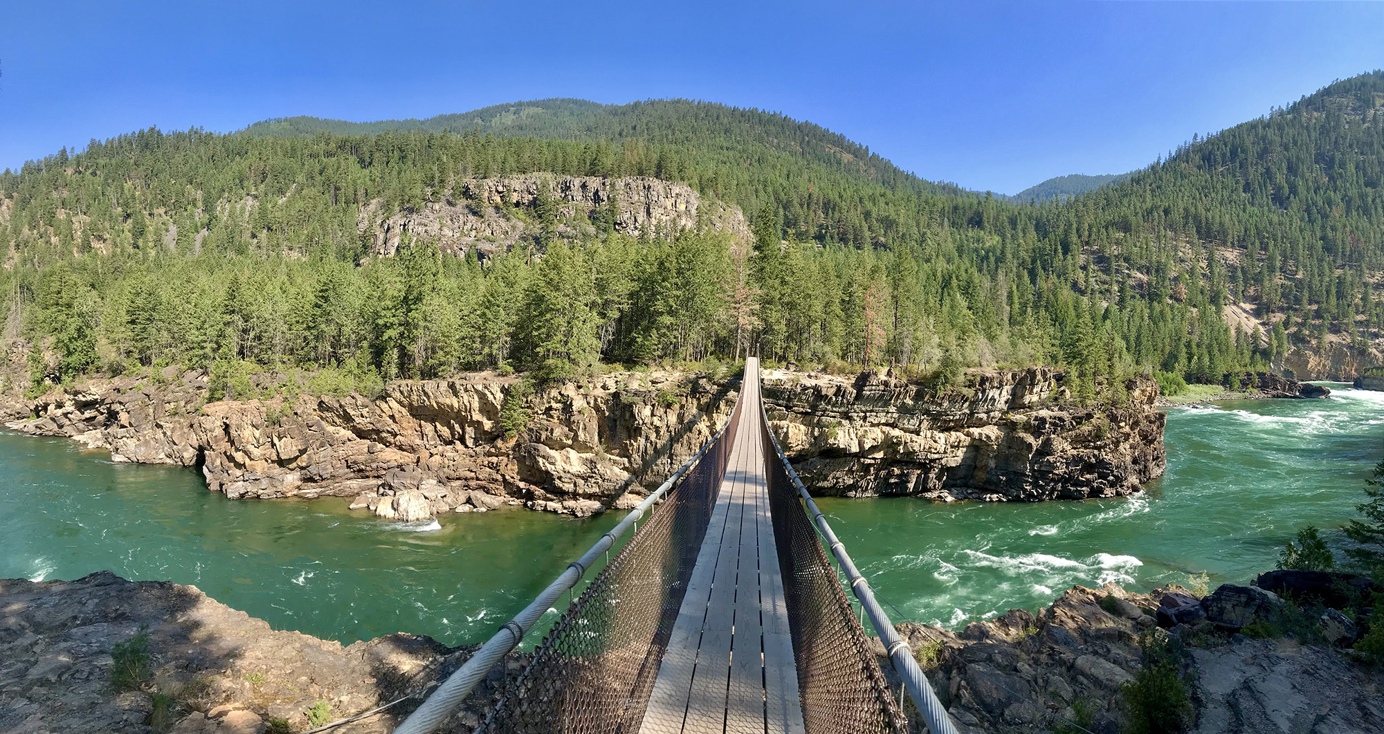 A swinging bridge stretches across a deep river gorge. 