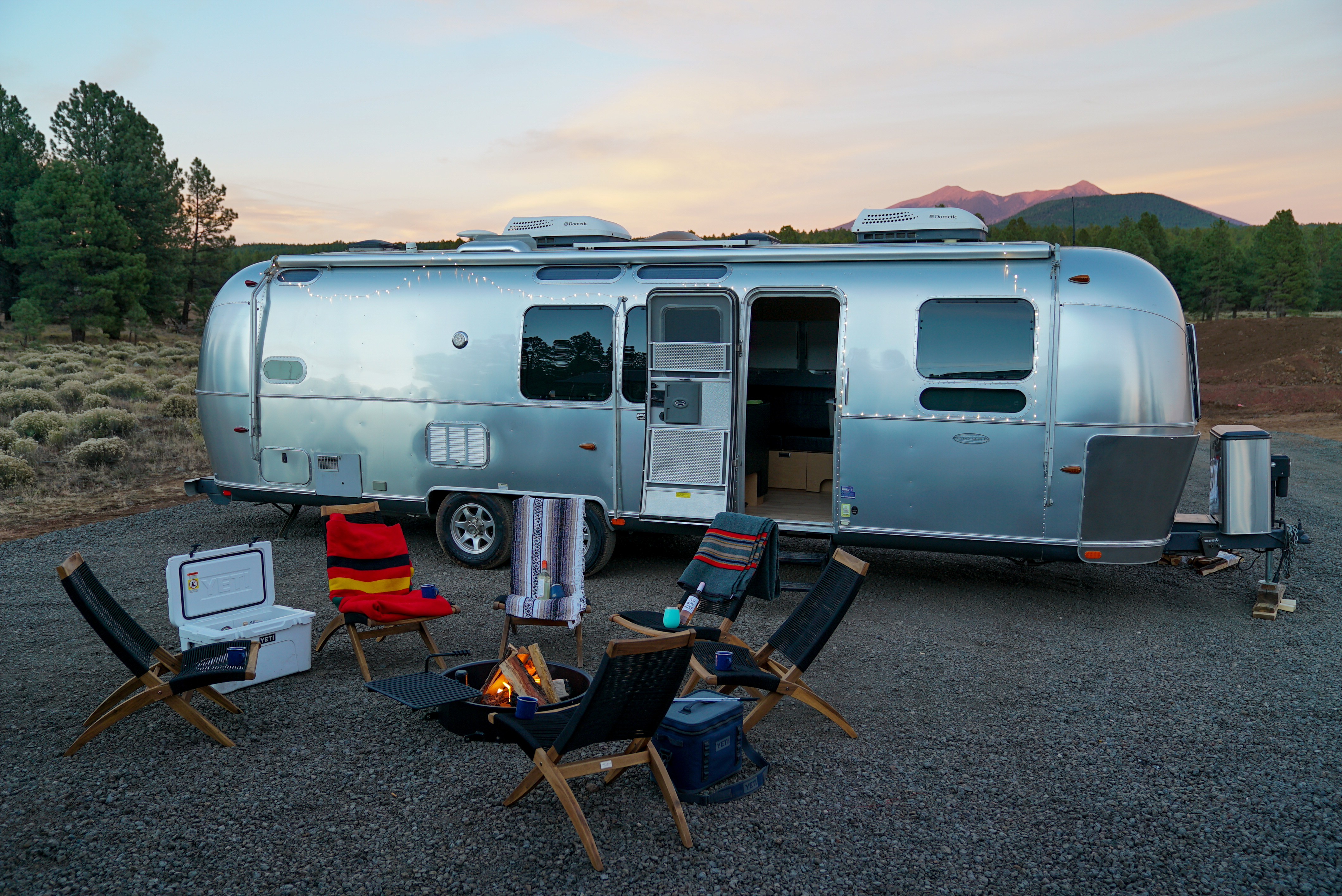 A lone Airstream trailer parked near a campsite with fire.