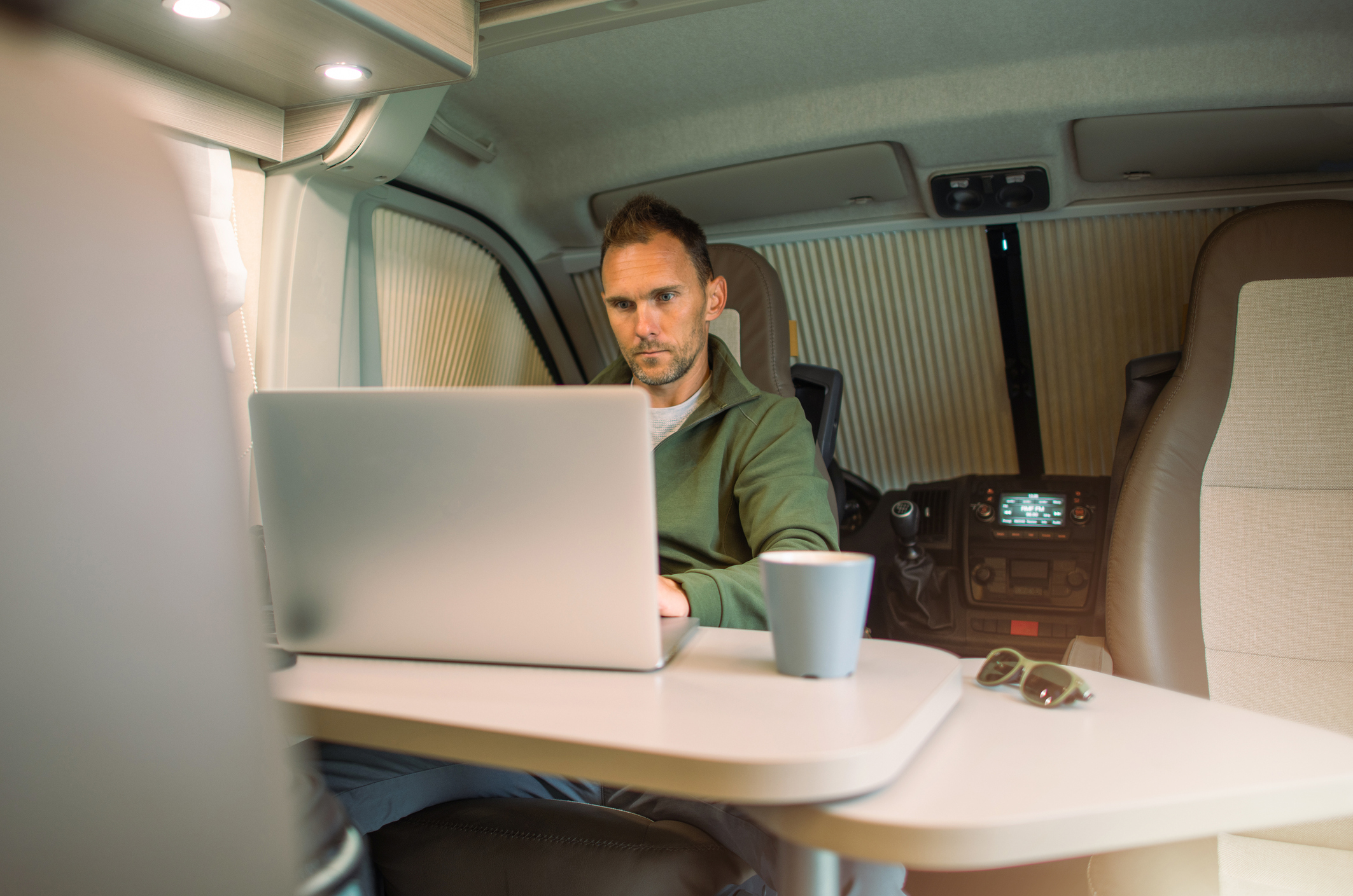 Caucasian Men in His 40s Working on His Computer Straight From His Camper Van While on a Road Trip. Remote Working Theme.