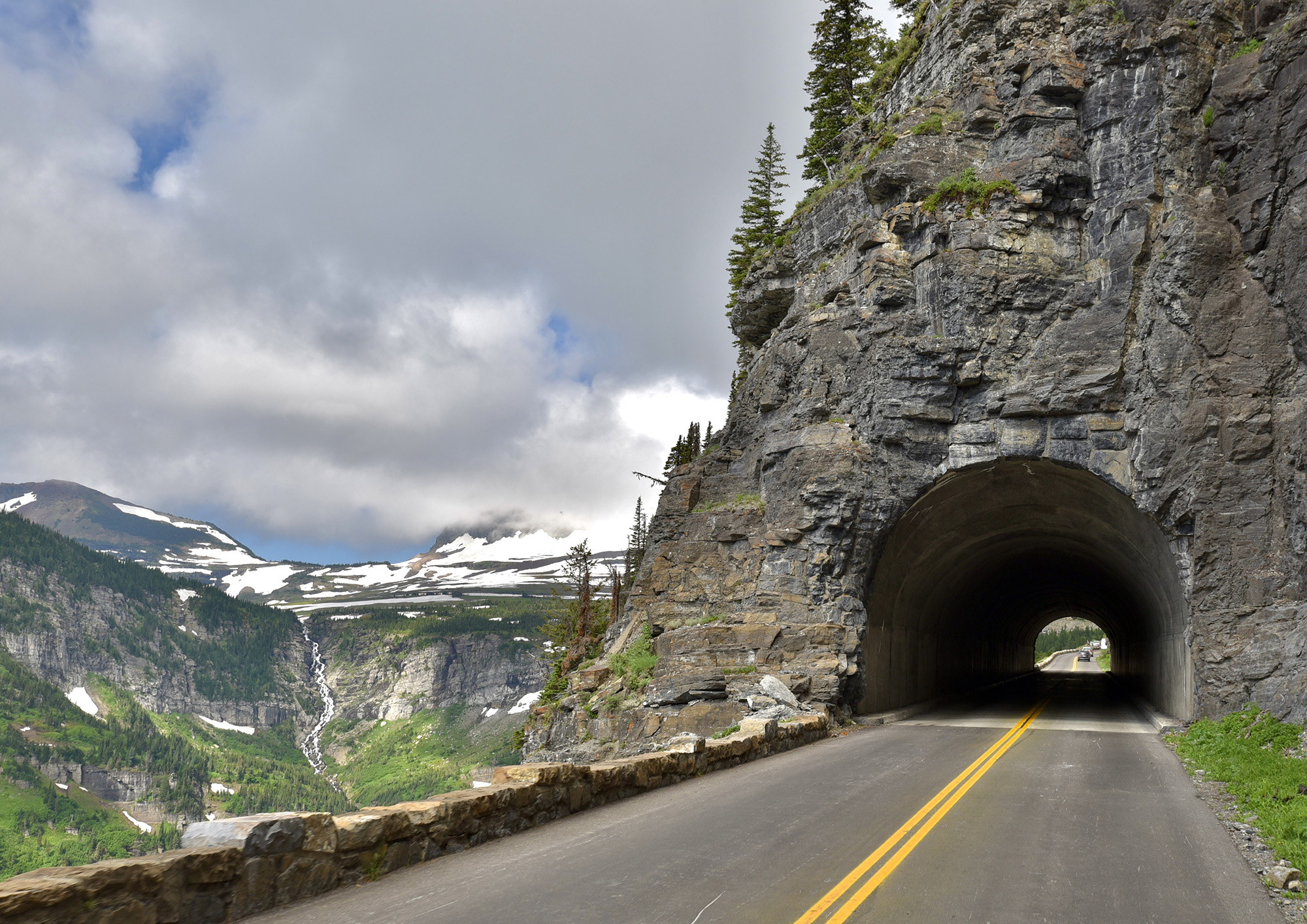 A tunnel cuts through a mountain on a road climbing an alpine slope. 