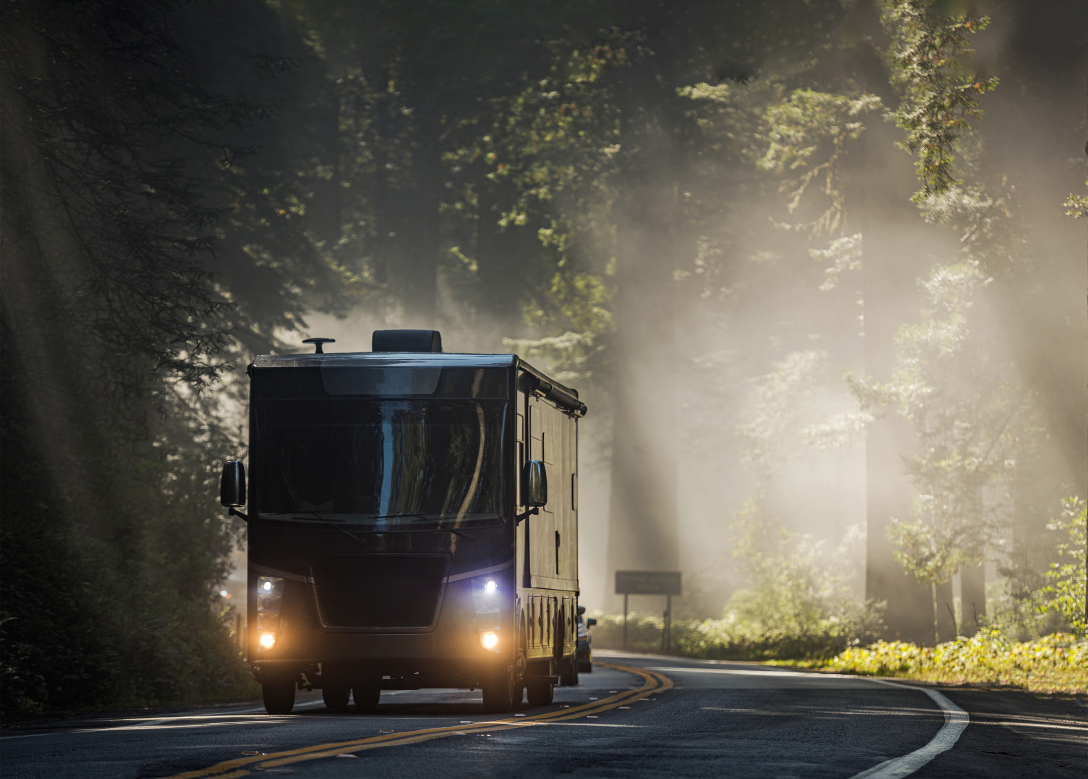 Motorhome driving through forest of tall redwoods.