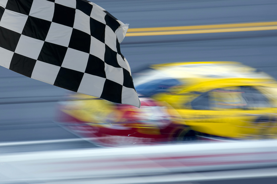 Blurred race car with flag in foreground.
