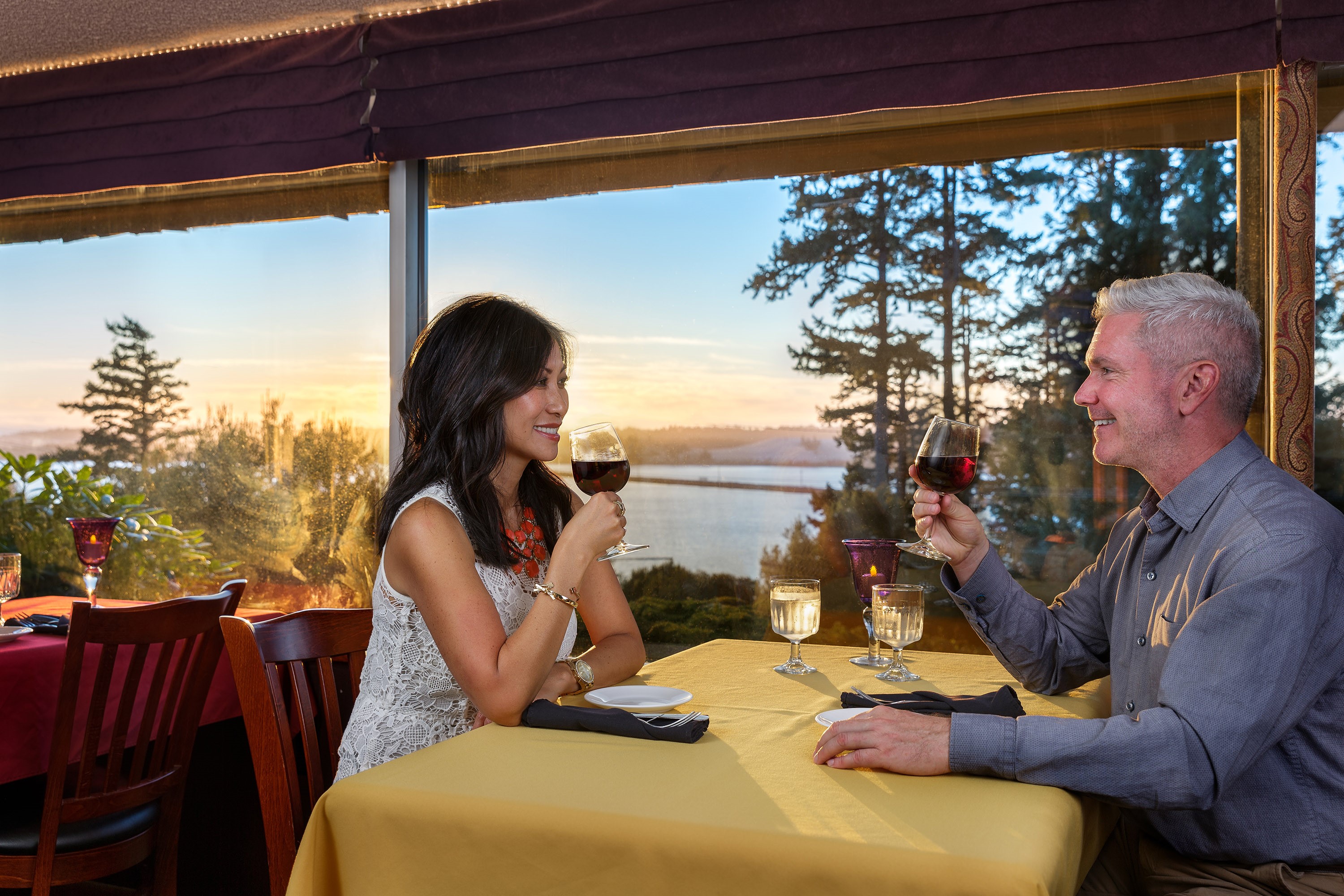 A couple enjoy a glass of wine in a restaurant with a window that looks out over a scenic coastal area.