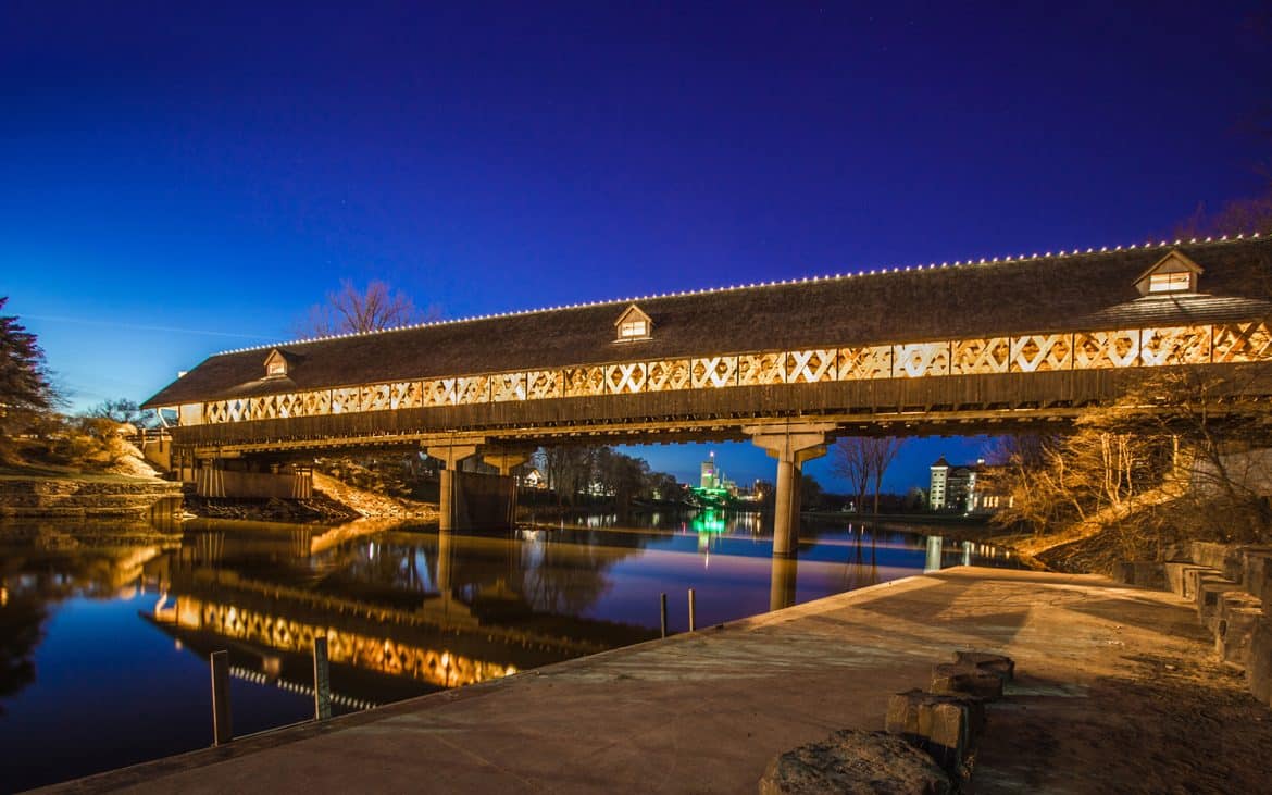 A wooden covered bridge spanning a river at night.