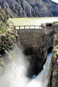 Water gushes out of the chute of a towering dam.