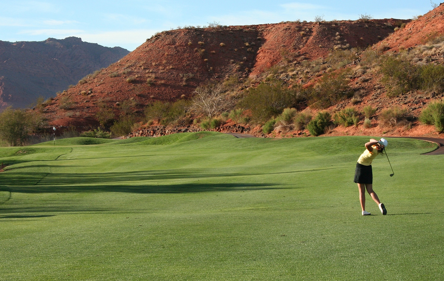 Woman takes a golf shot on desert golf course.
