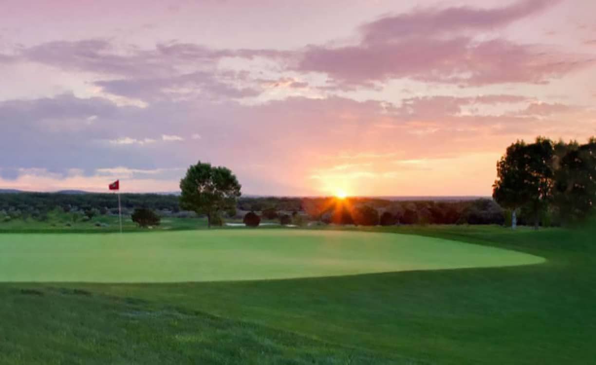 Sun sets over a golf green surrounded by lush trees.