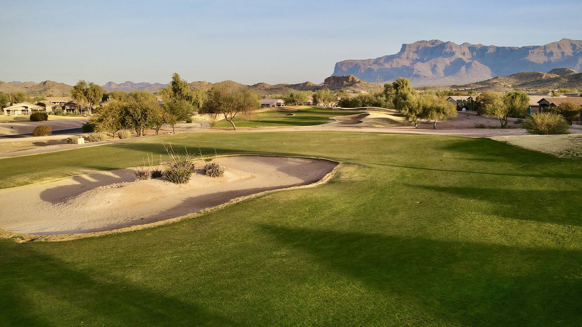 Lush golf course with sand traps and rocky mountains in the background.