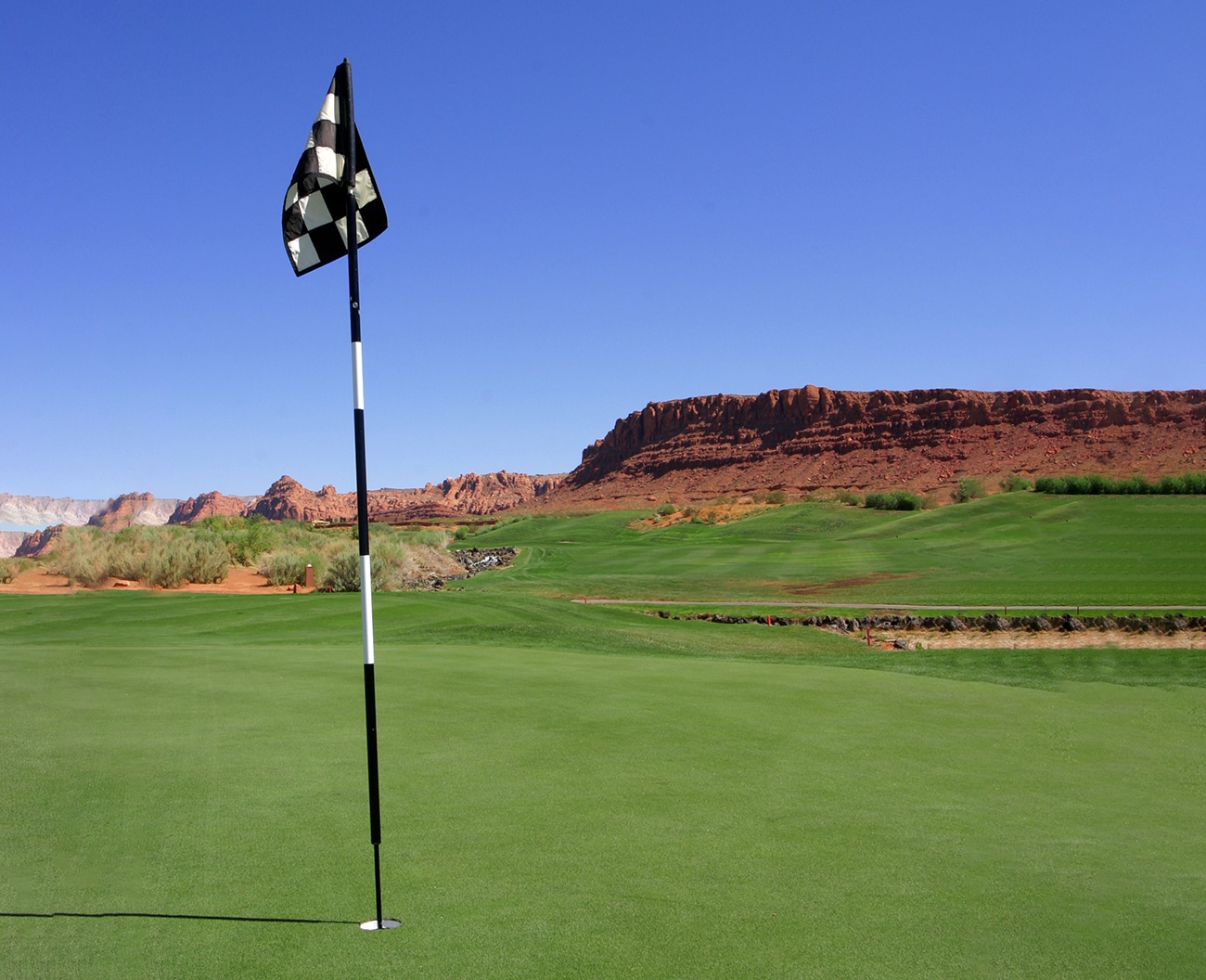 A golf course with red rock bluff in the background.