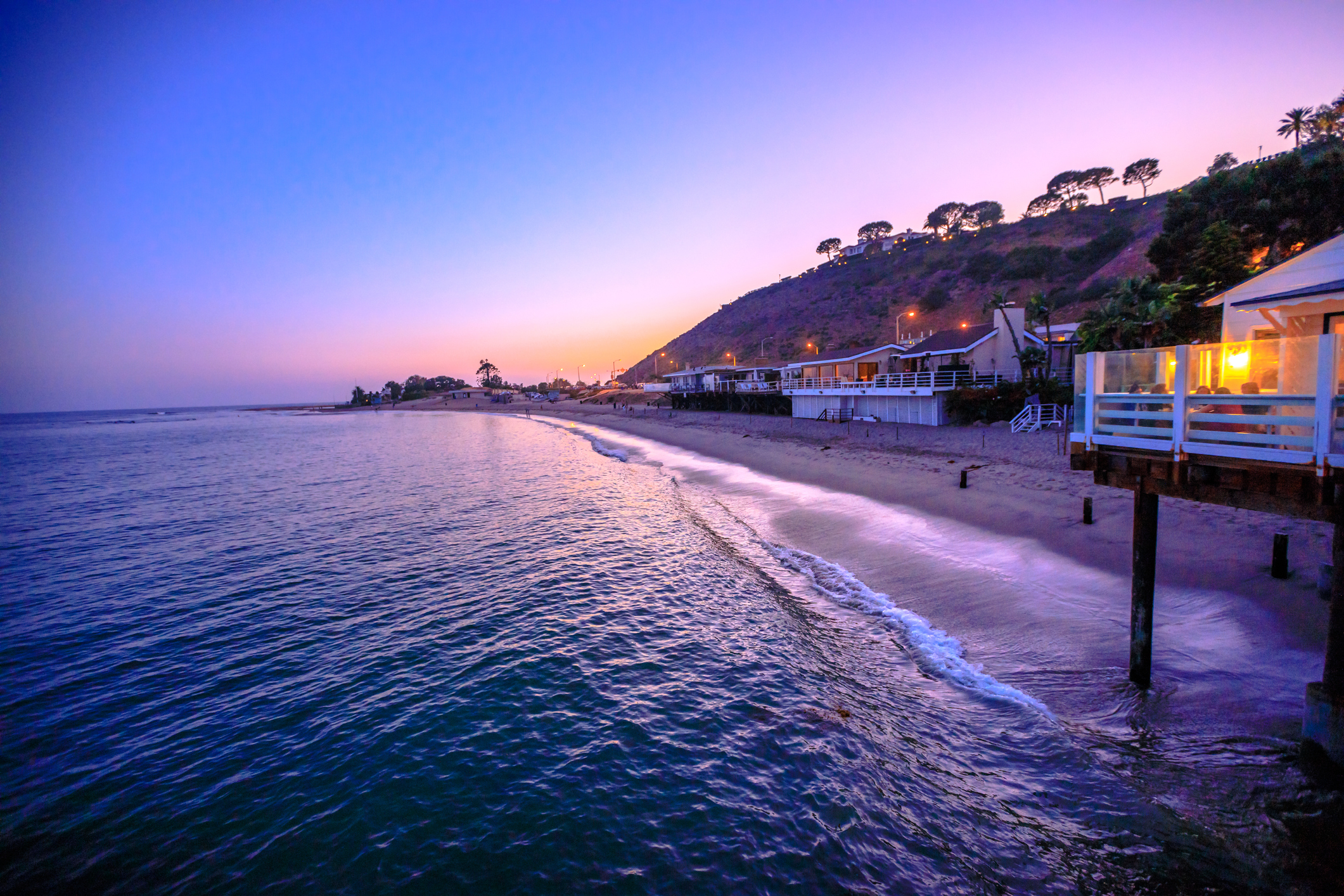 Beach houses line the shore of a coast at dusk.