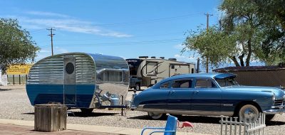 Sedan with a bullet-shaped trailer under a blue sky at an RV park.