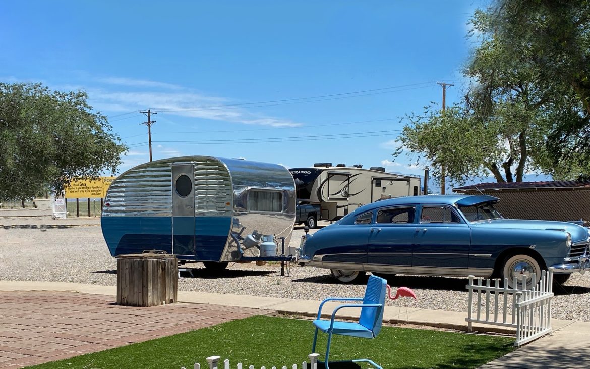 Sedan with a bullet-shaped trailer under a blue sky at an RV park.