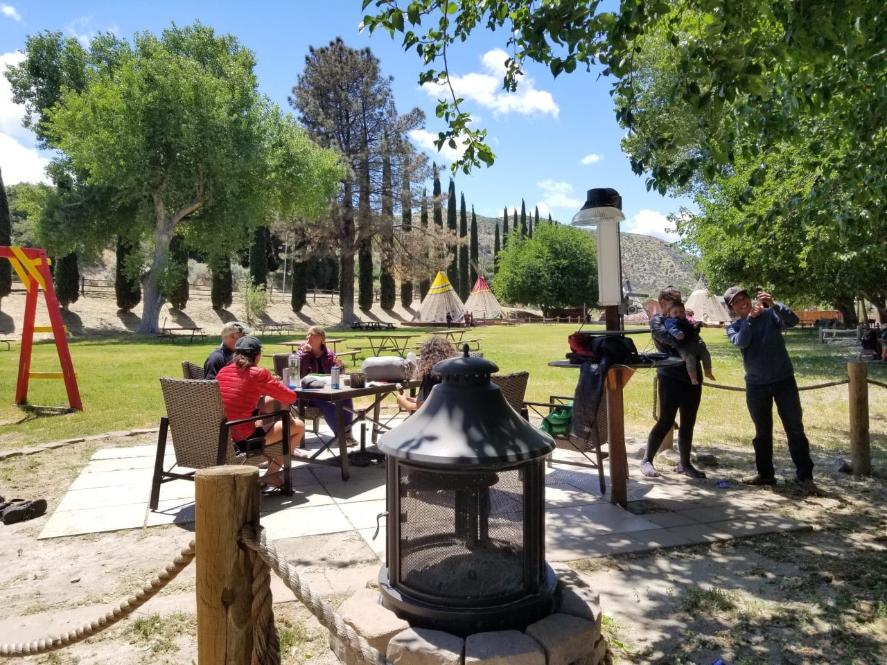 Campers relaxing at a picnic table with with tepees in the background.