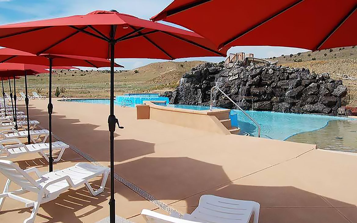 Red umbrellas cast shade on deck chairs overlooking a pool in a desert setting