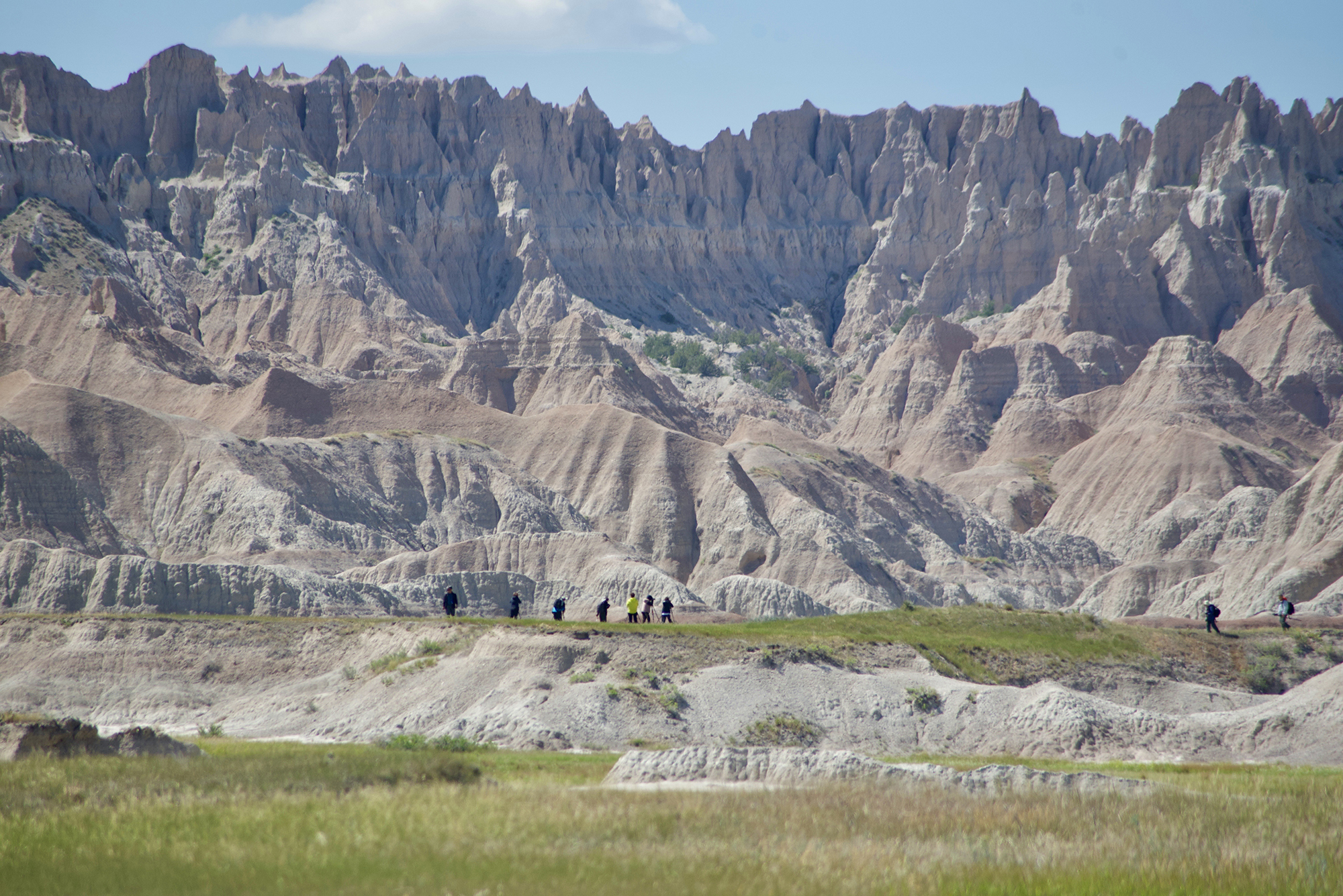 Hikers are dwarfed by Badlands that tower in the horizon.