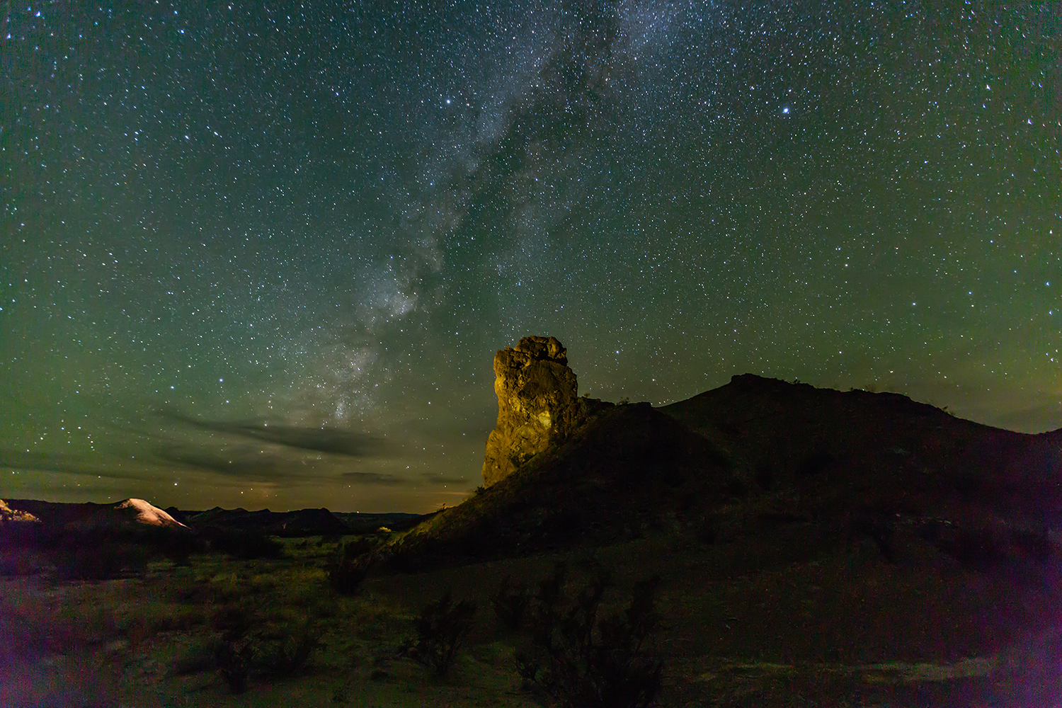 Stars twinkle over a rock outcropping in the desert.