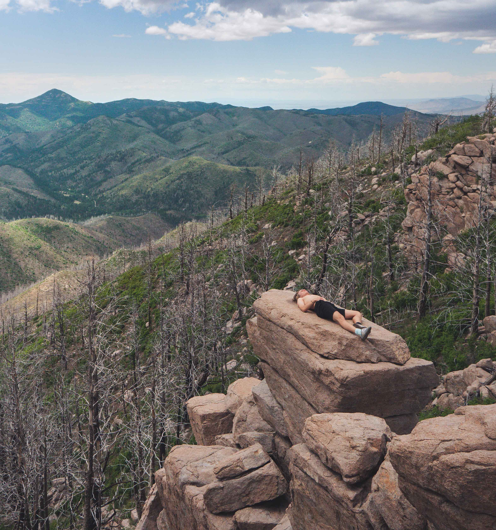 A lone hiker relaxes on a high rock outcroppingn overlooking a deep mountain valley.