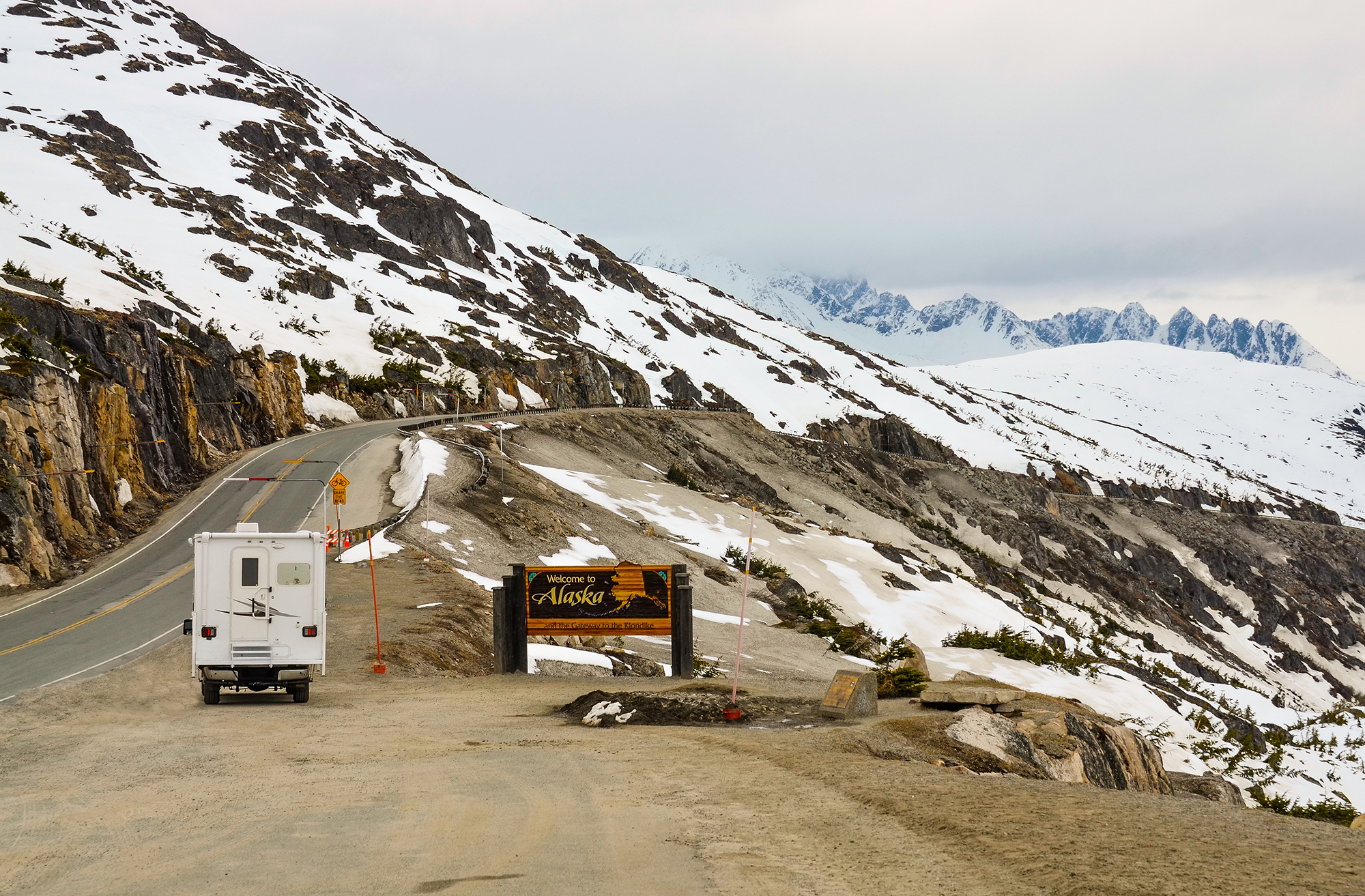 RV About to tackle incline hugging a snowy ridge.