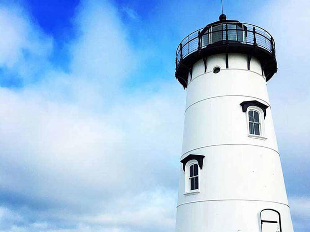 A white lighthouse risees against a cloudy sky.