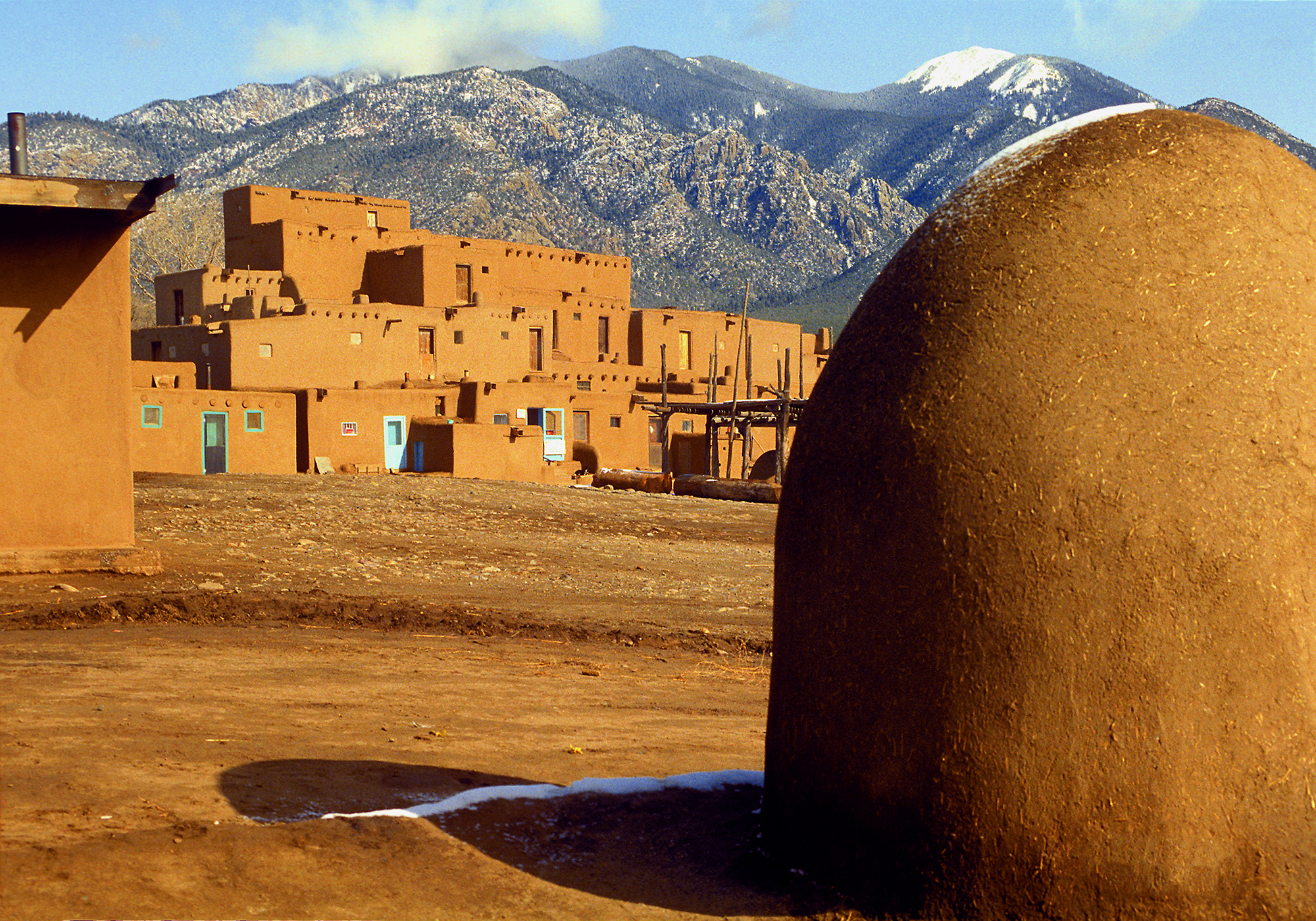 An ancient pueblo building with a backdrop of snow-covered mountains.