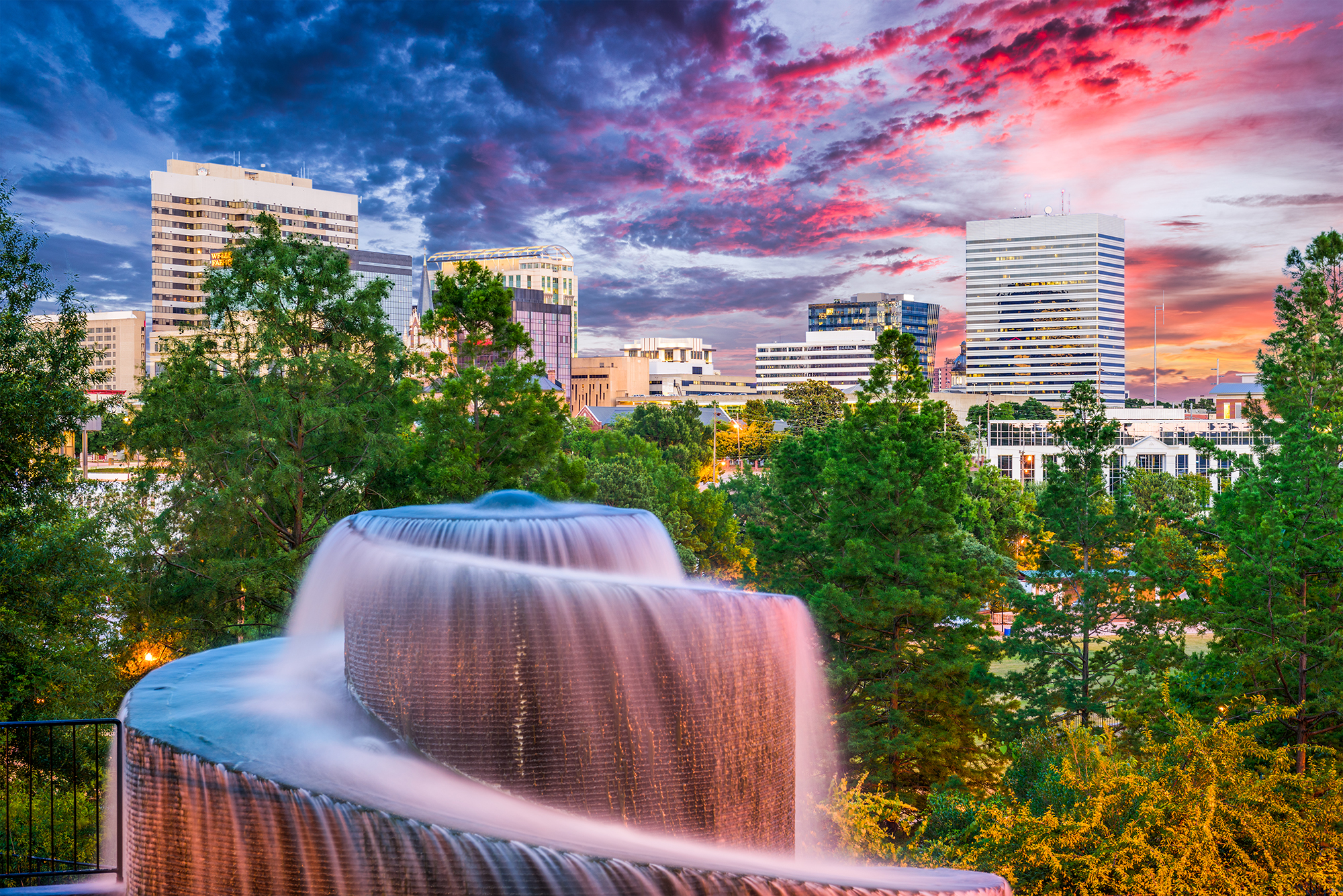 Spiral fountain in foreground with tall buildings in background.