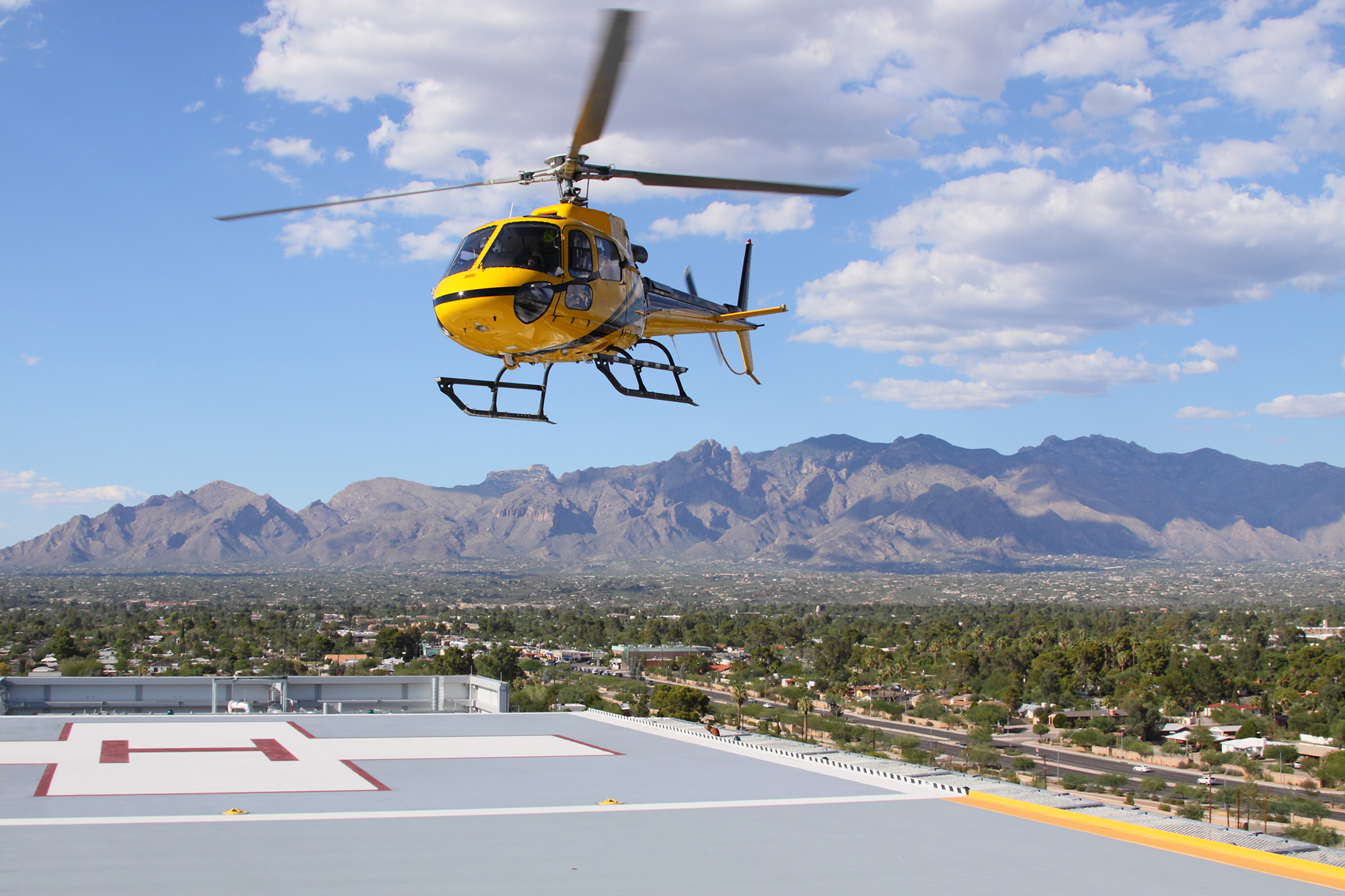 A yellow rescue helicopter lands on a hospital landing pad.