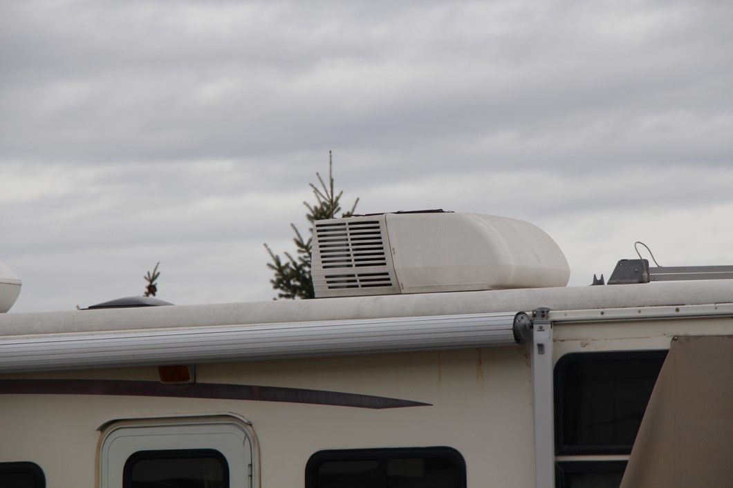 RV roof air conditioning unit under gray sky.