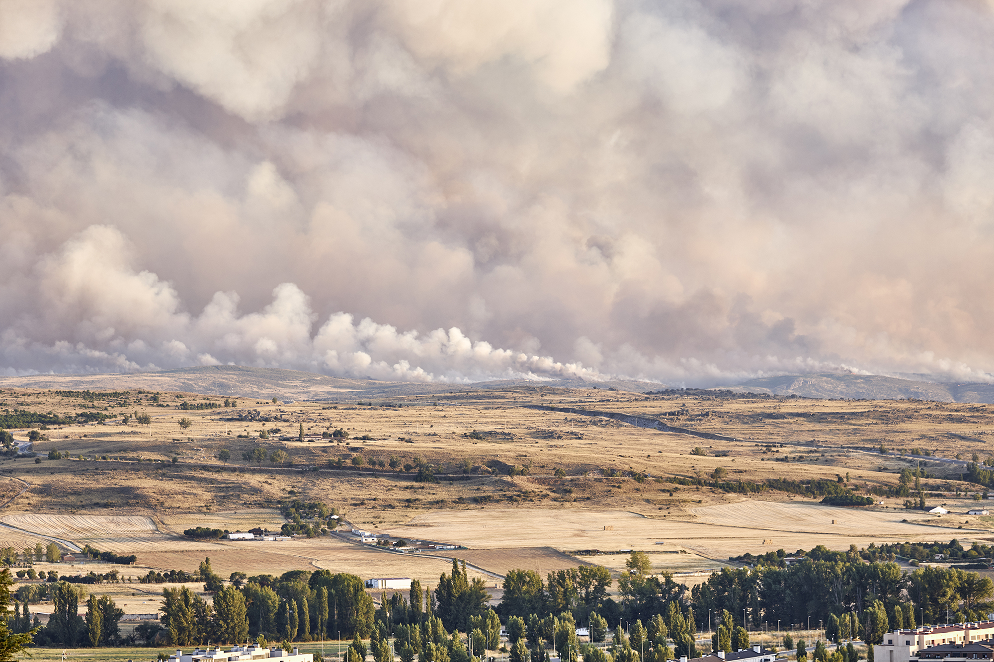 Photograph of a large forest fire with a large column of smoke on a hillside near a city. Natural disaster concept