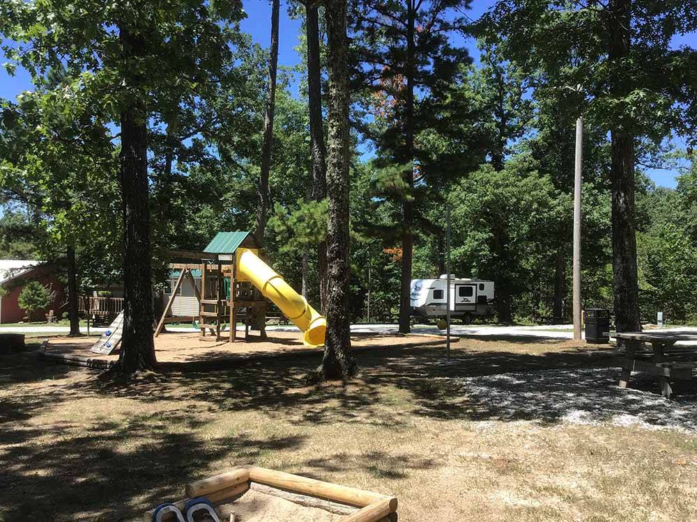 Playground in foreground with RVs in background amid wooded setting.