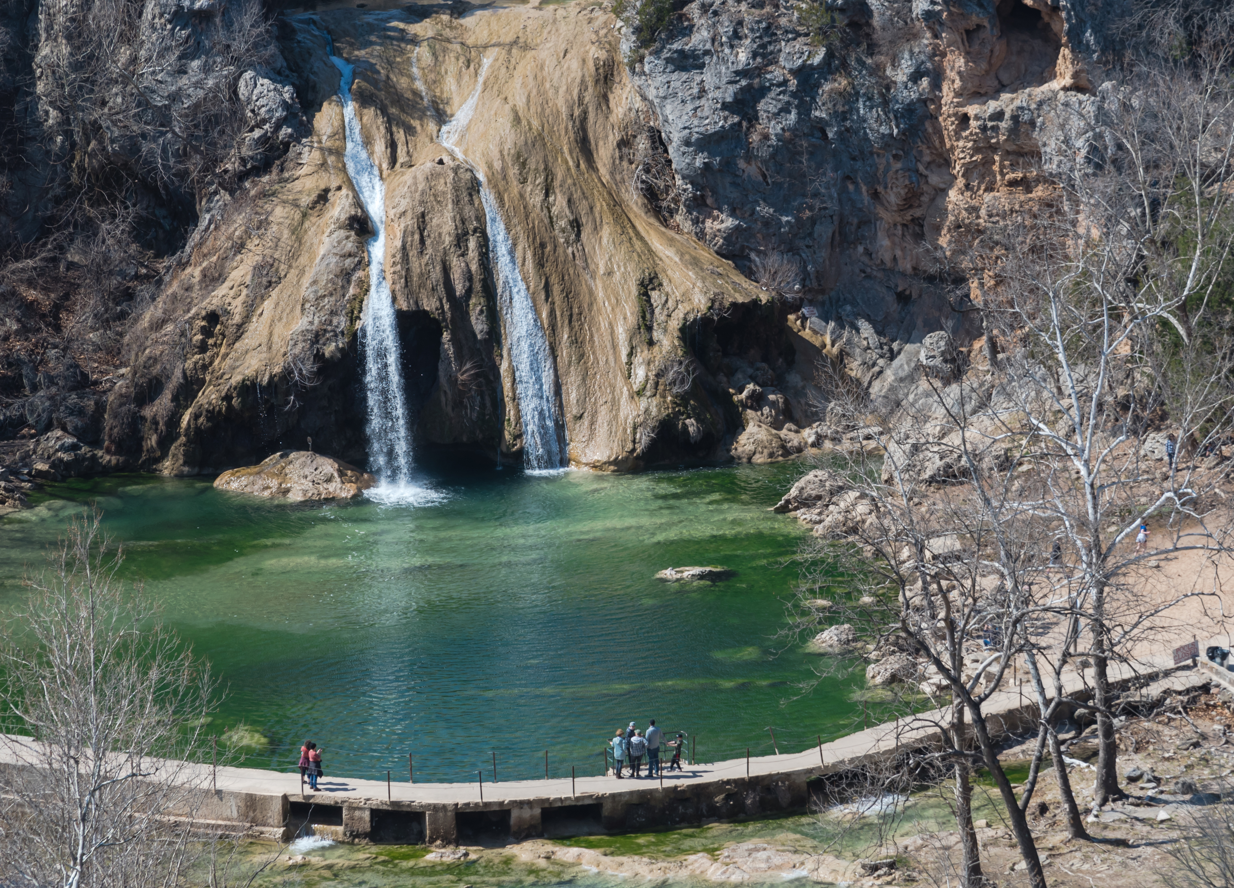 A waterfall empties into an emerald pool as spectators watch.