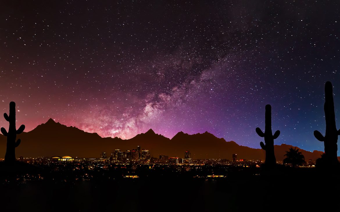 Starry sky over cityscape with cacti silhouettes in foreground.
