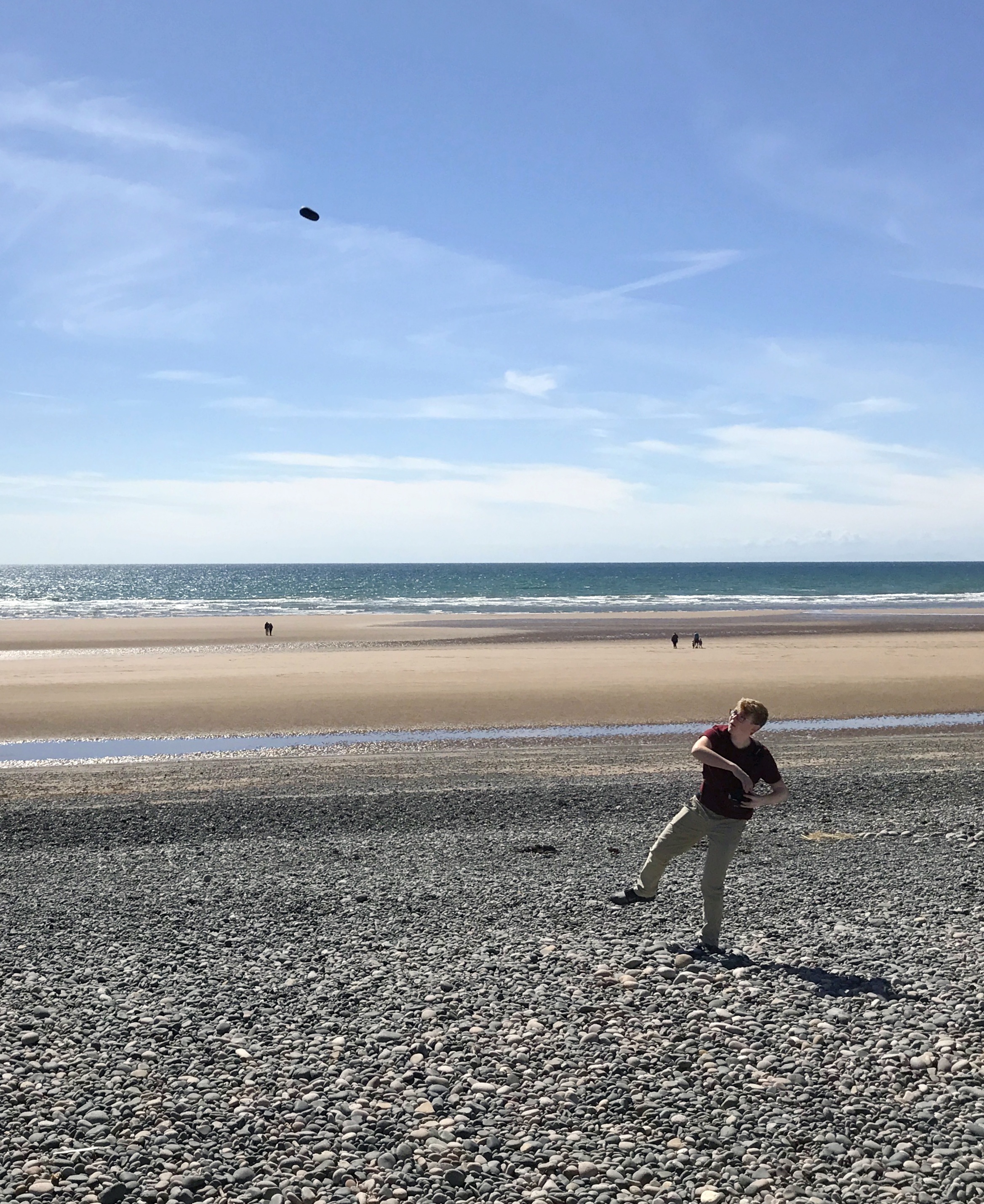 Teenager throwing rock on rocky beach.