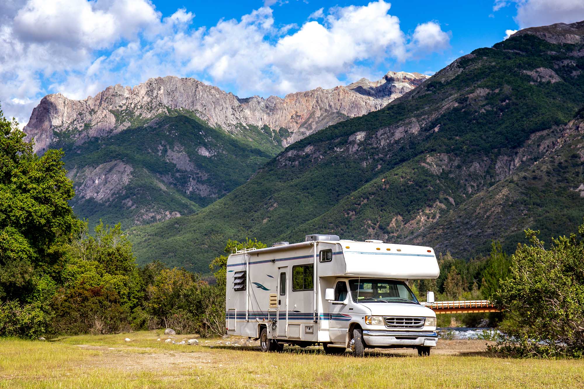 A truck camper parked at a site with towering mountains in background.