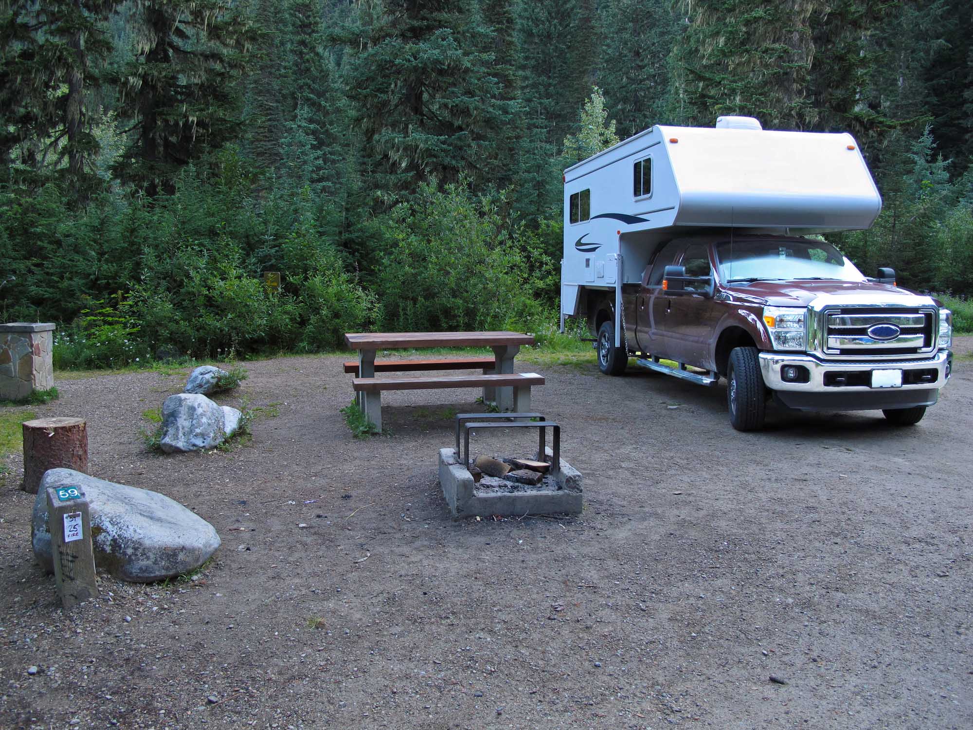 Truck camper parked on dirt campsite.