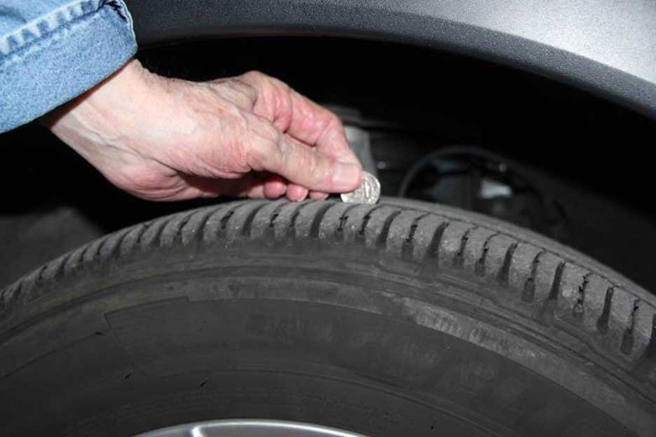 Man places a quarter on the tread of a tire to gauge depth of tread.