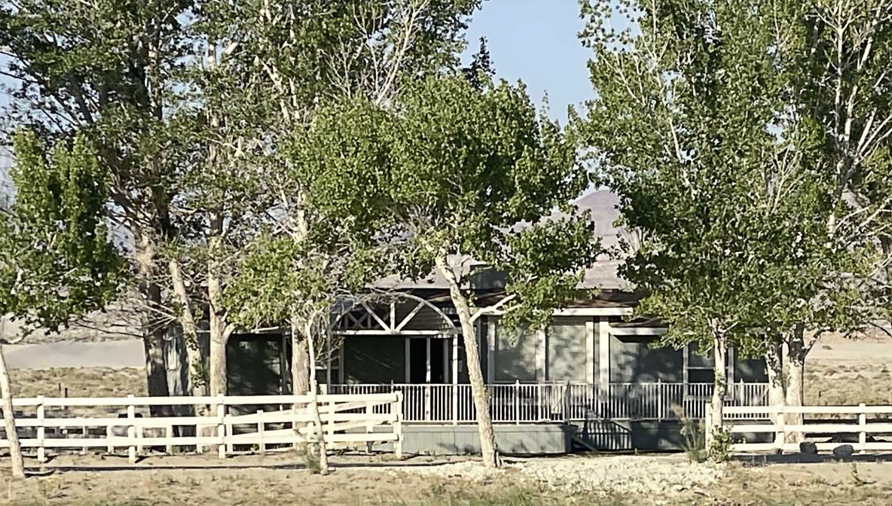 A house behind wooden fence and shielded by tall, leafy trees.