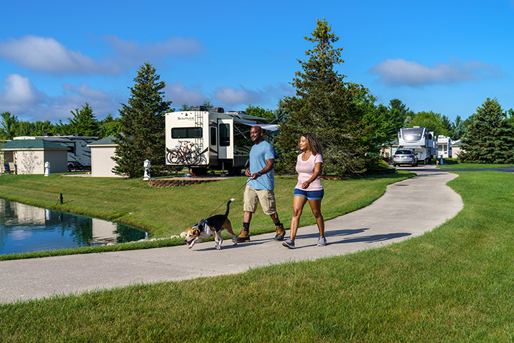 A couple walking their dog on a paved path.