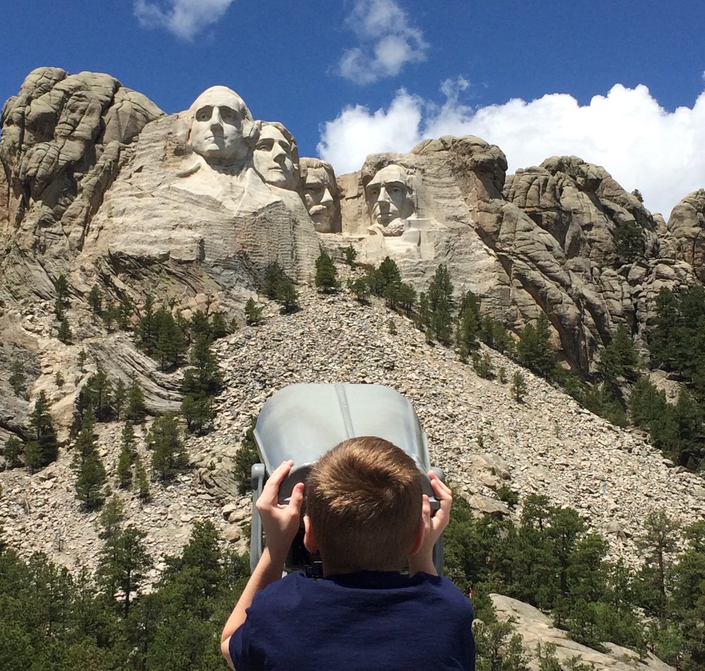 Jovem olha para o Monte Rushmore através de um telescópio.