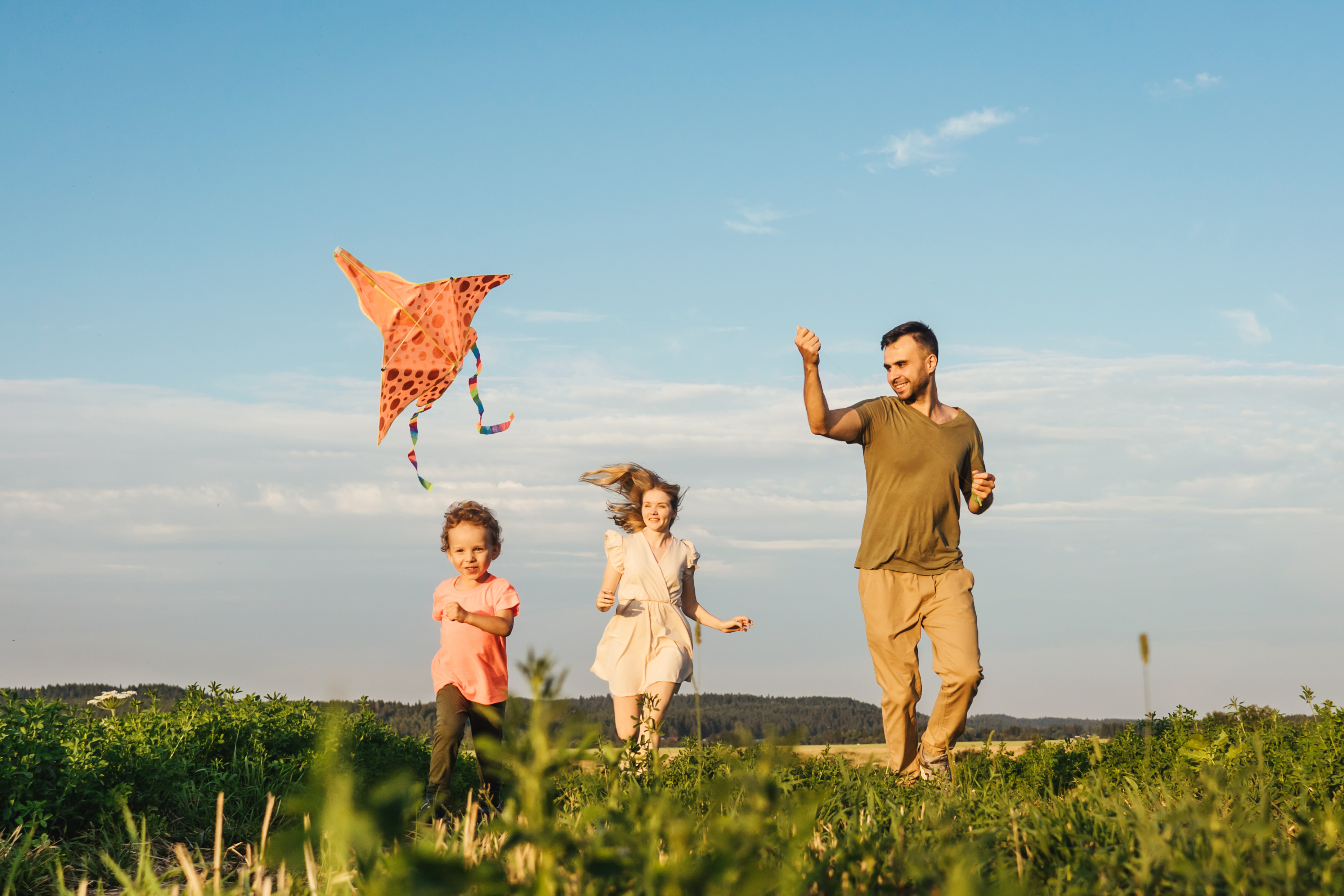 Young happy family with little boy run in field and flying a kite.