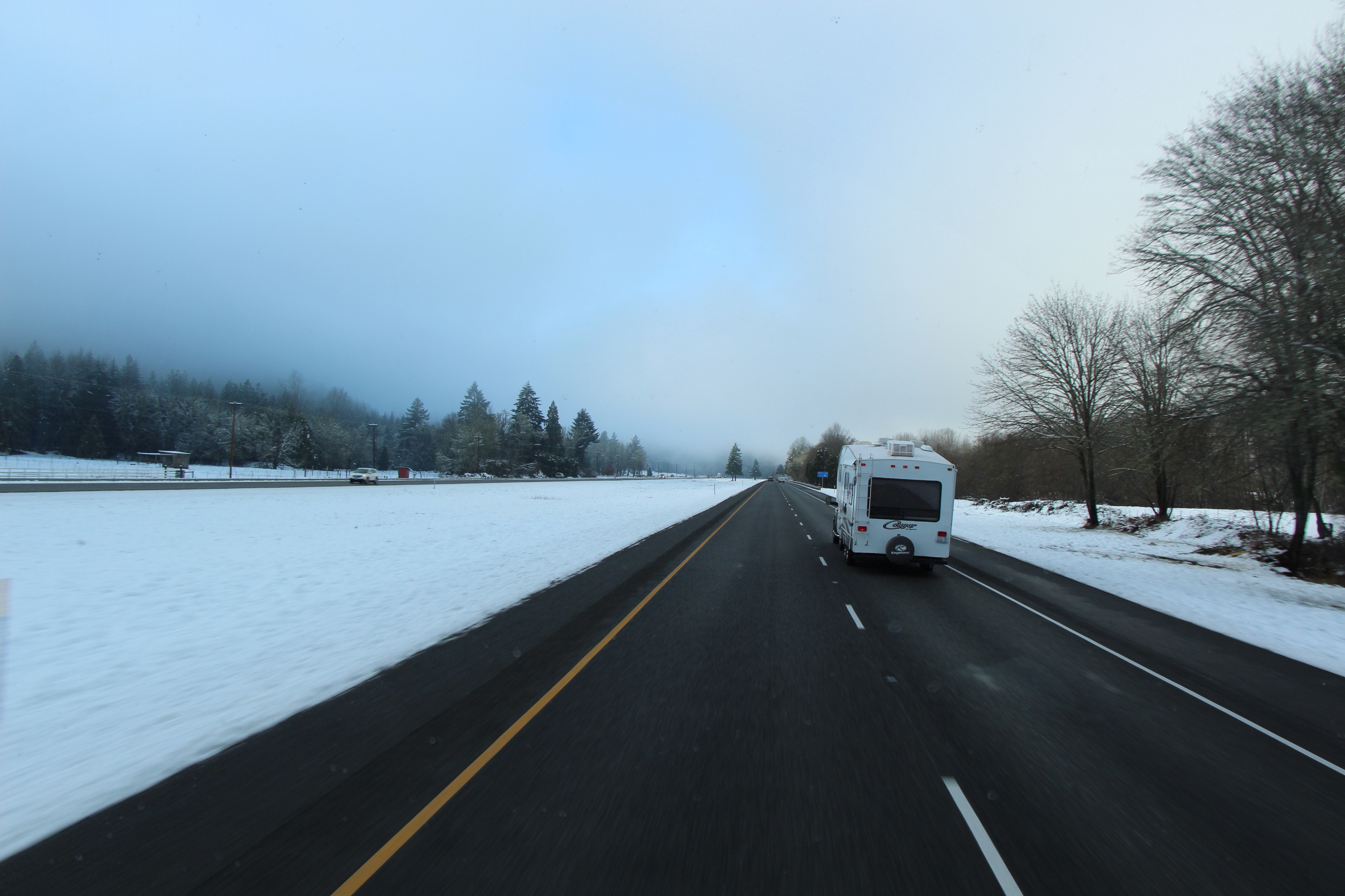 A fifth-wheel drives down a highway flanked with snow banks.