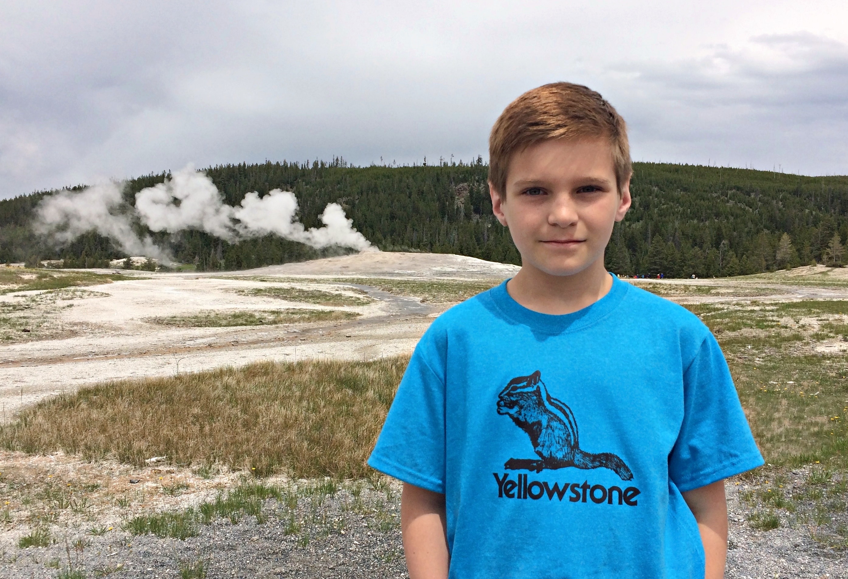 Young man stands in front of geyser.