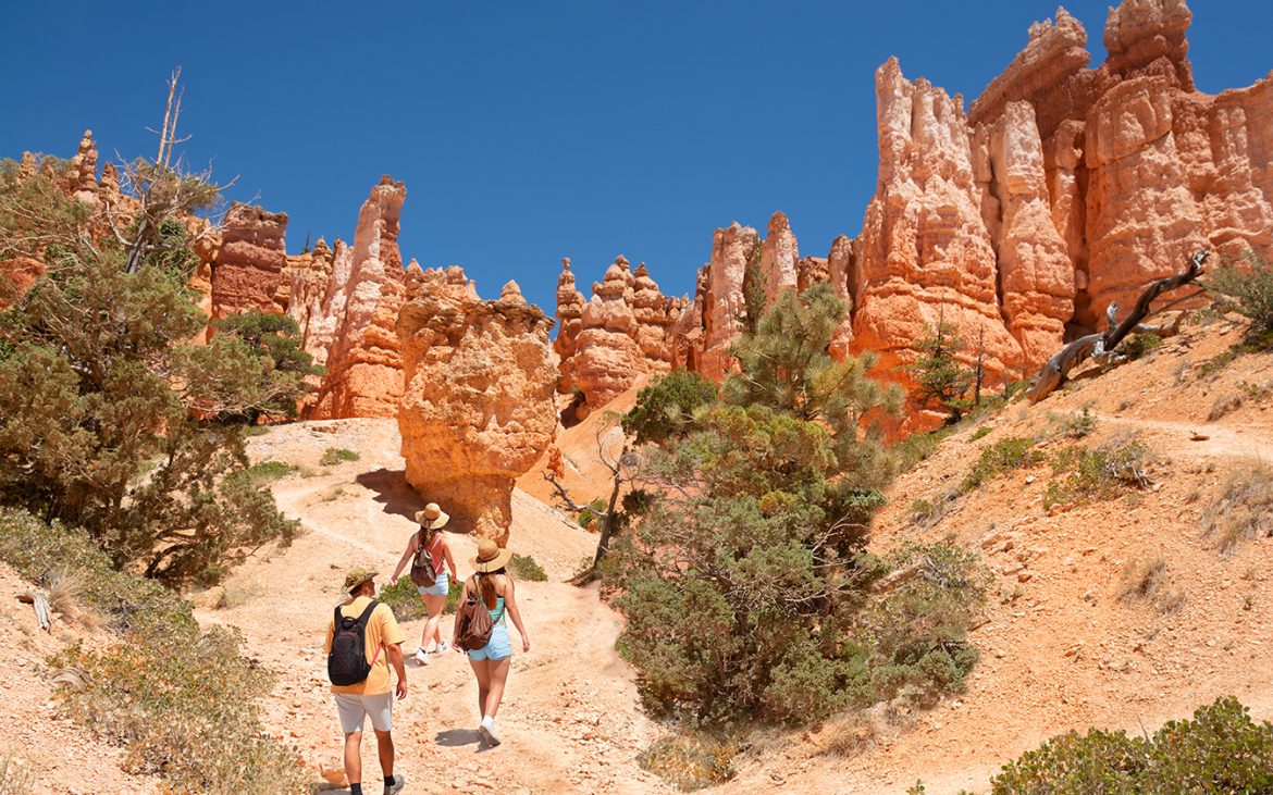 A trio of hikers ascend a slope toward craggy rock arches.