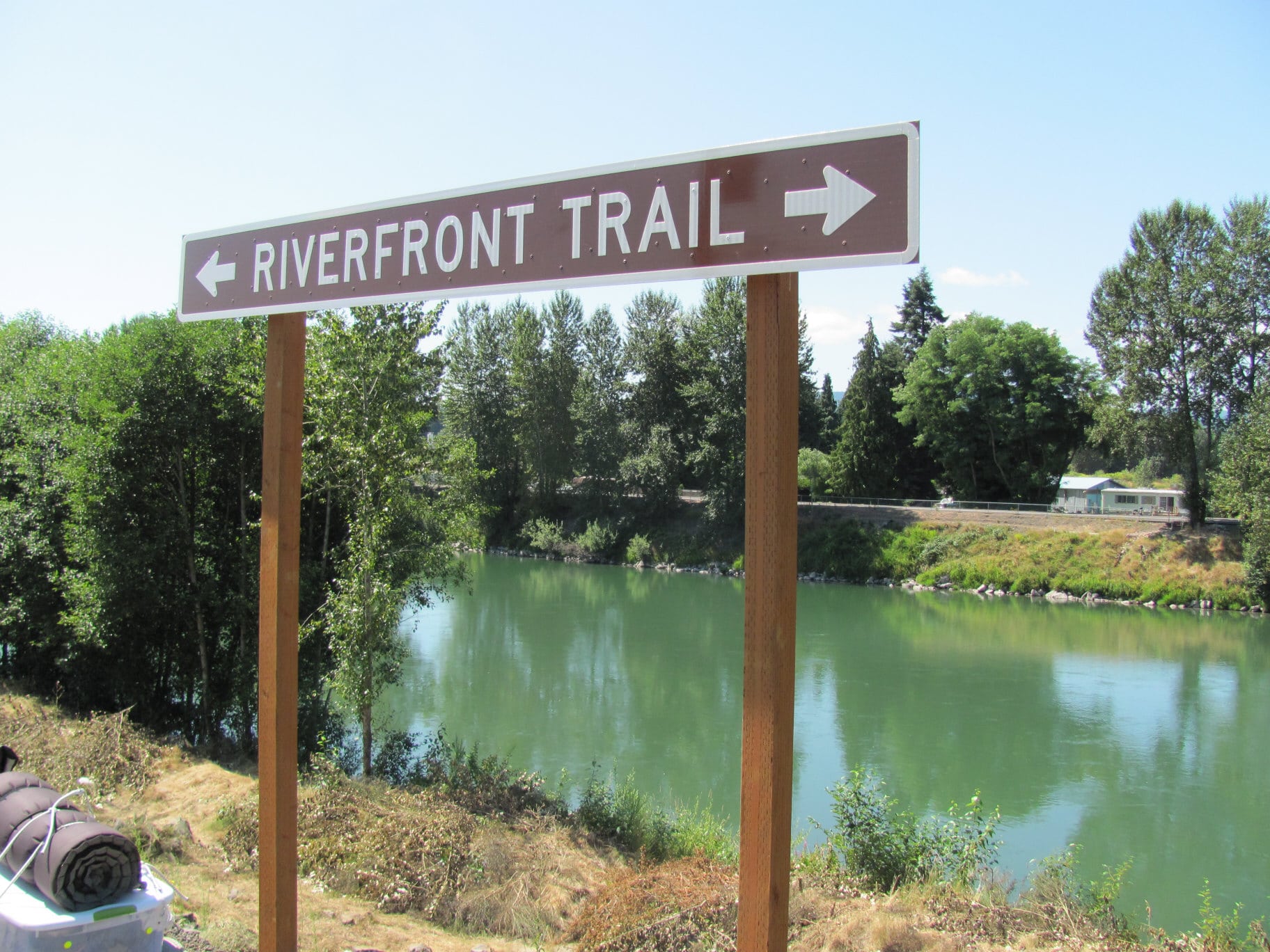 A sign proclaiming "Riverfront Trail" in front of a river.