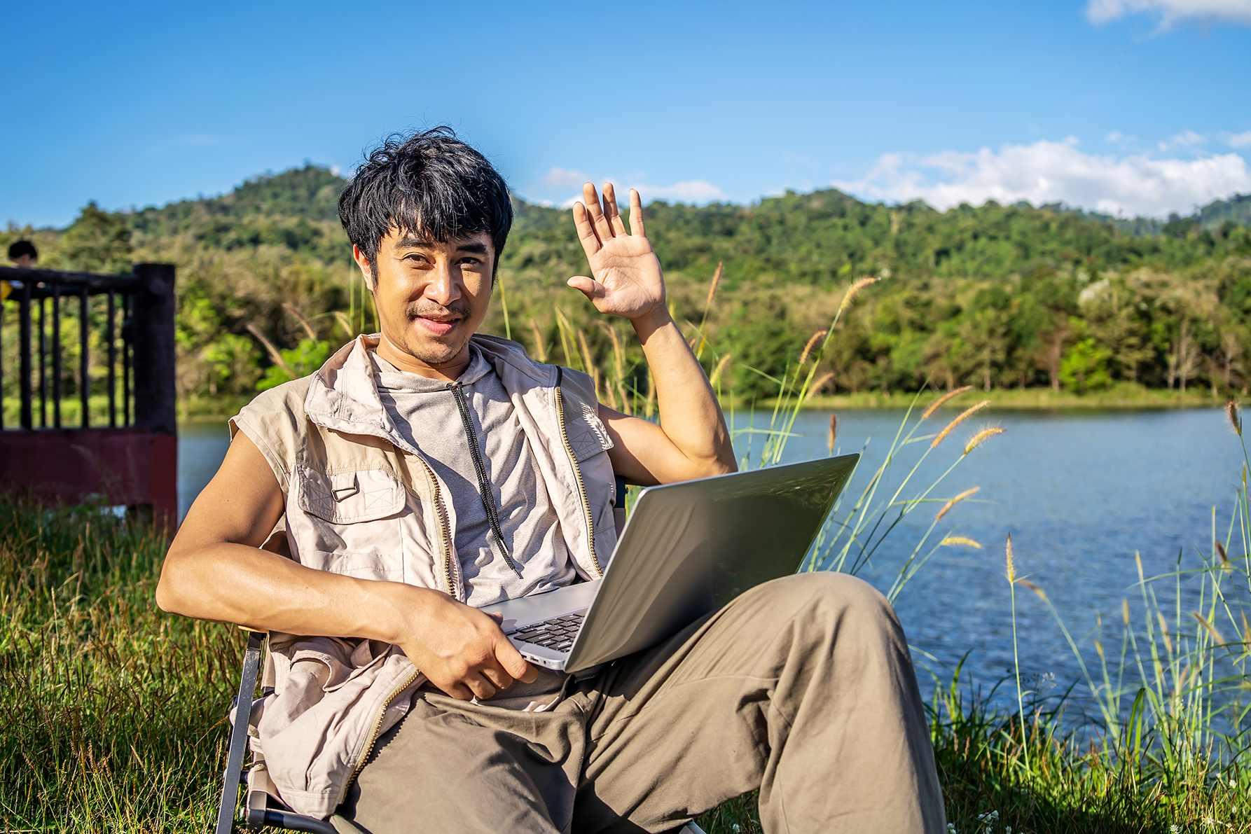 Young man near a lake at a campground with laptop.