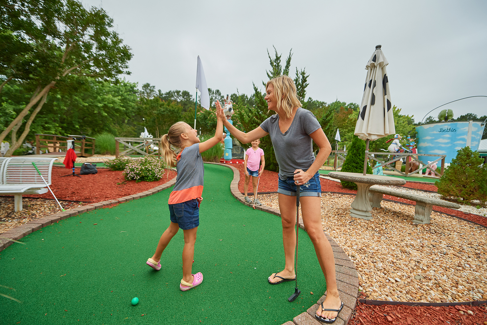 Woman and young girl high five in miniature golf course.